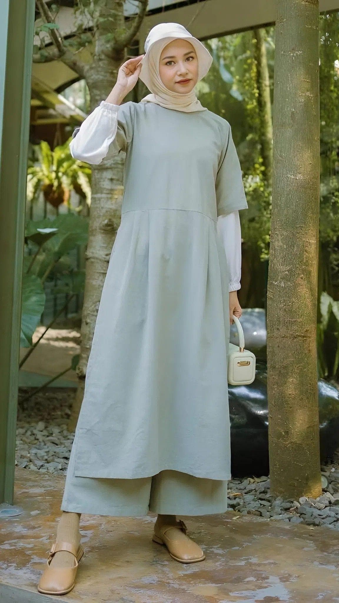 A modest linen dress set with attached white inner sleeves, worn with matching linen pants in an outdoor garden setting.