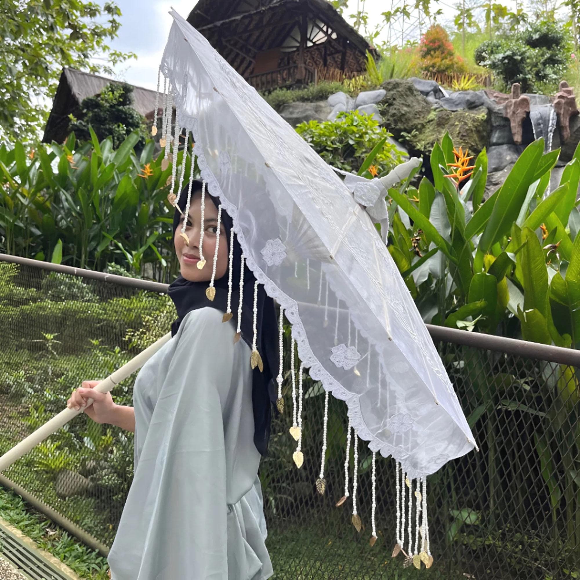 Large white embroidered bridal parasol with beaded fringe displayed outdoors in a garden setting