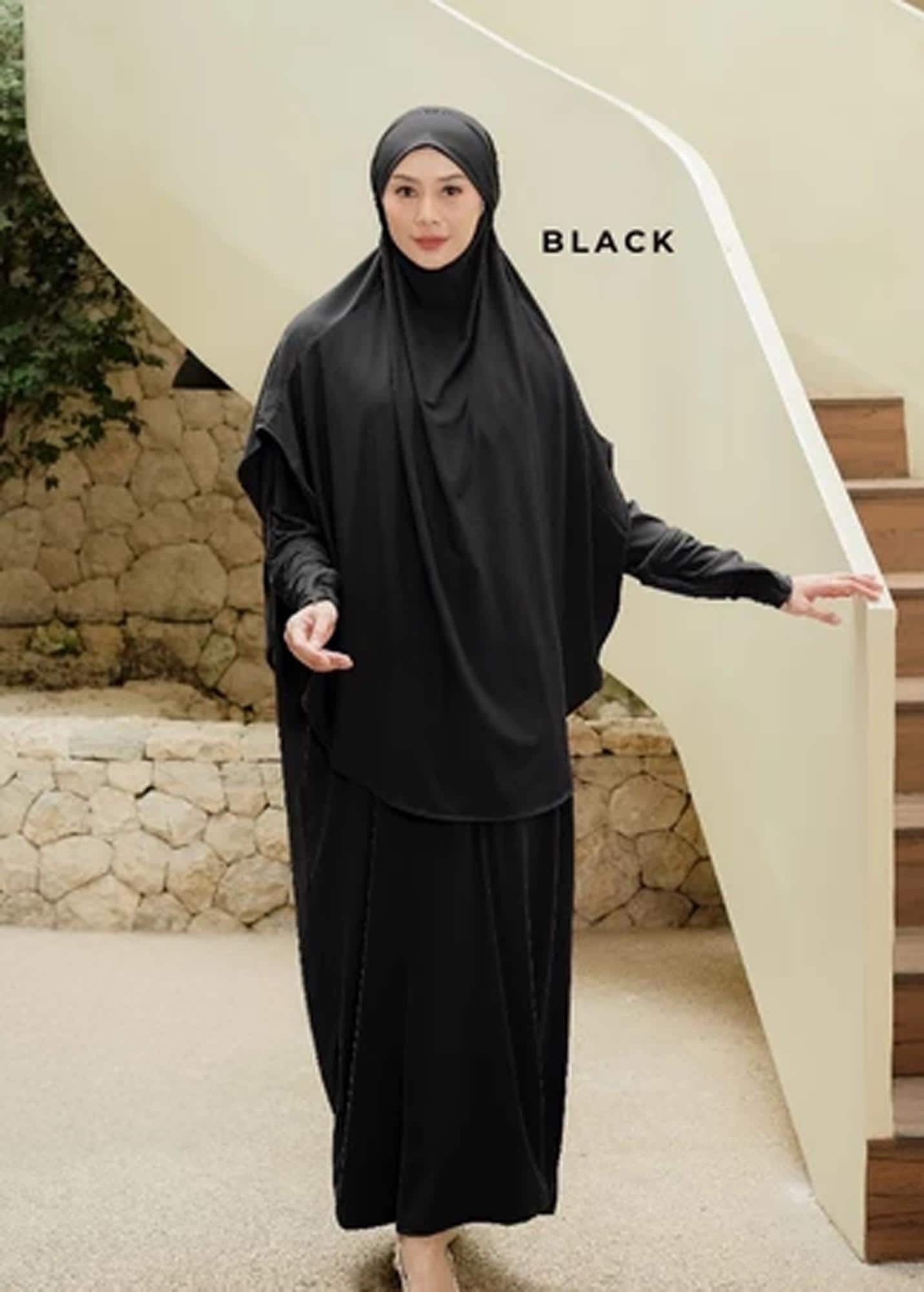 An oversized dark grey jersey abaya set with a matching long khimar worn by a woman in a minimalist setting.