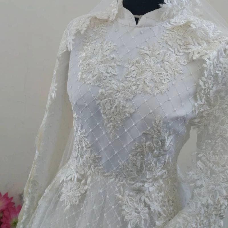 White embroidered lace wedding dress with long sleeves, floral appliqué, and flowing tulle skirt displayed on a mannequin.