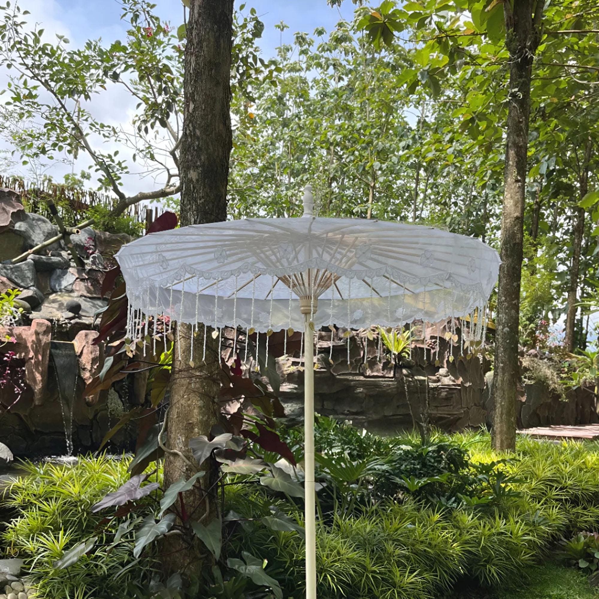Large white embroidered bridal parasol with beaded fringe displayed outdoors in a garden setting