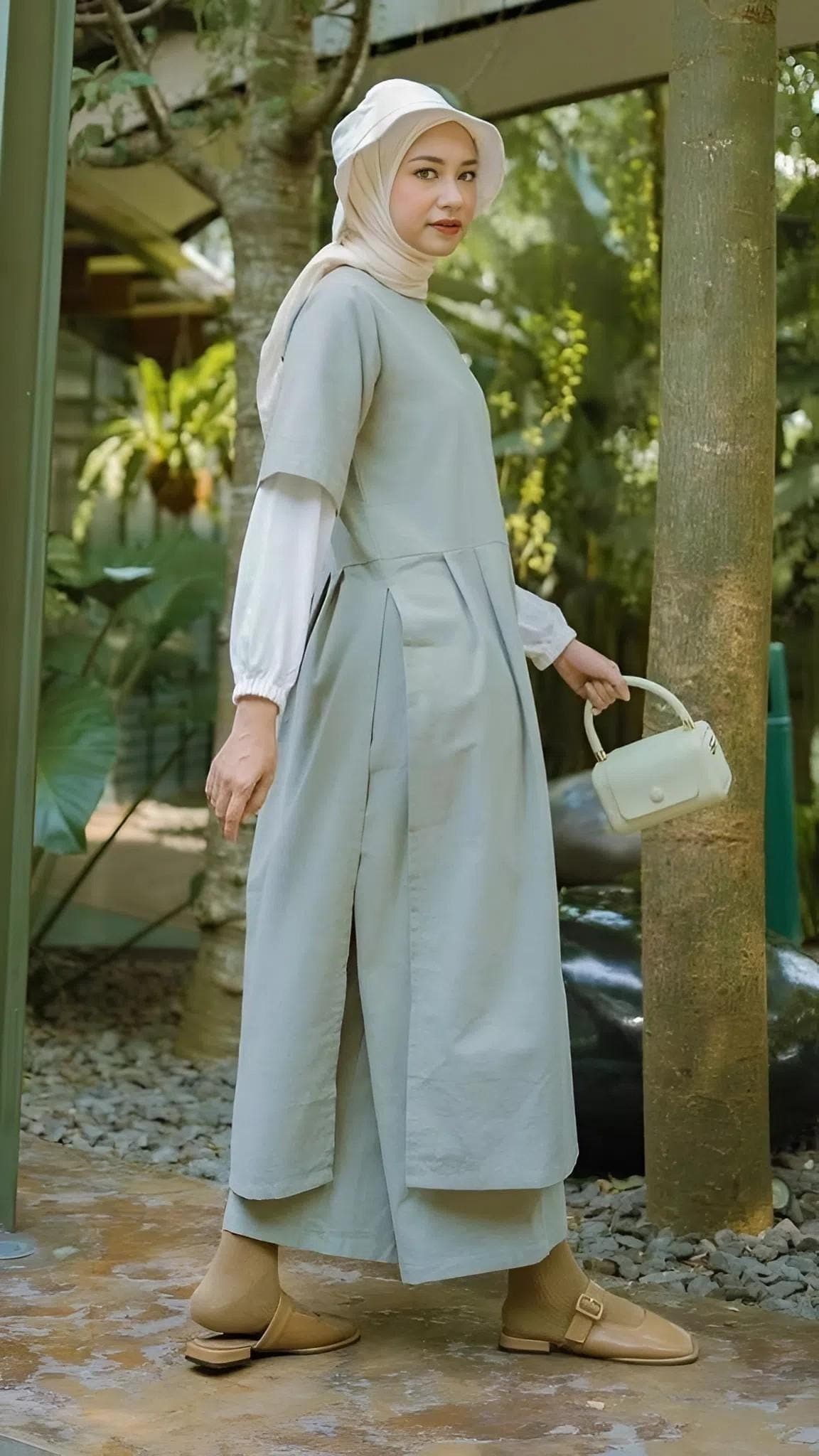 A modest linen dress set with attached white inner sleeves, worn with matching linen pants in an outdoor garden setting.
