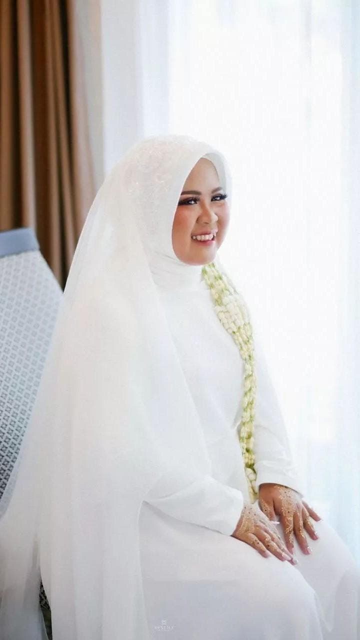 Minimalist white silk abaya wedding dress with flowing cape and matching hijab worn indoors, styled for a modest bridal look.