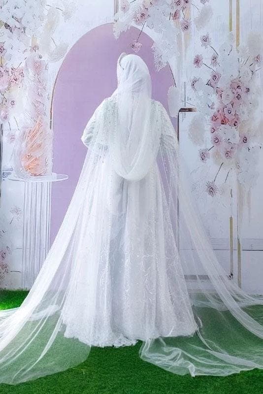 A modest satin and embroidered tulle wedding dress with long flowing skirt, pearl details, and matching veil displayed in a bridal studio.