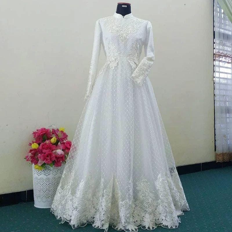 White embroidered lace wedding dress with long sleeves, floral appliqué, and flowing tulle skirt displayed on a mannequin.