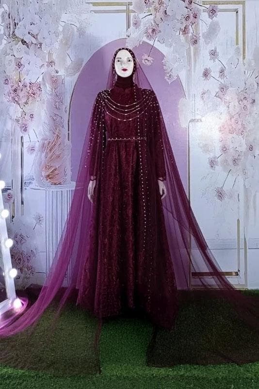 A modest satin and embroidered tulle wedding dress with long flowing skirt, pearl details, and matching veil displayed in a bridal studio.