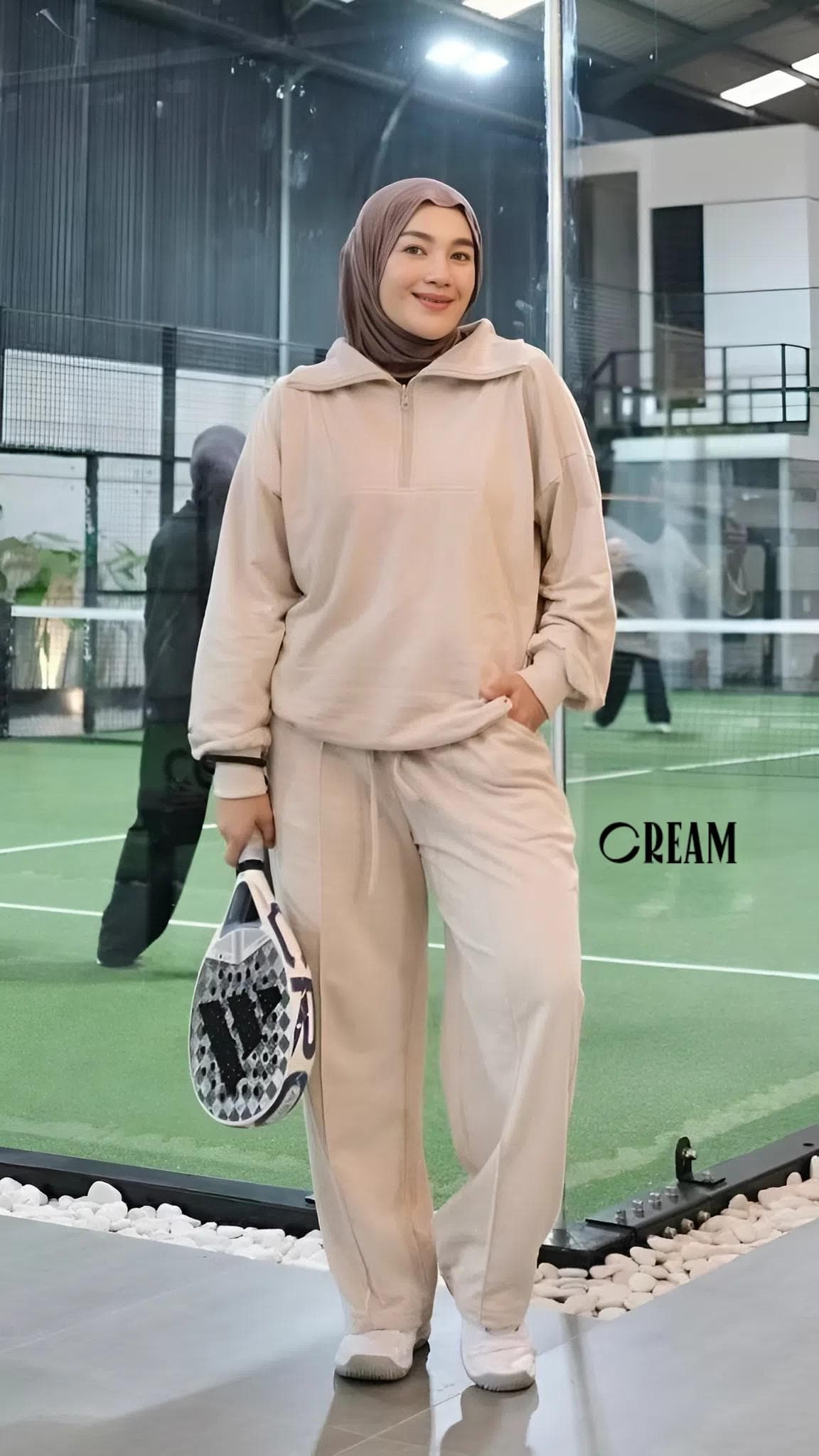 A modest women’s babyterry tracksuit set in dark smokey color, featuring a half-zip top and loose athletic pants, worn on an indoor sports court