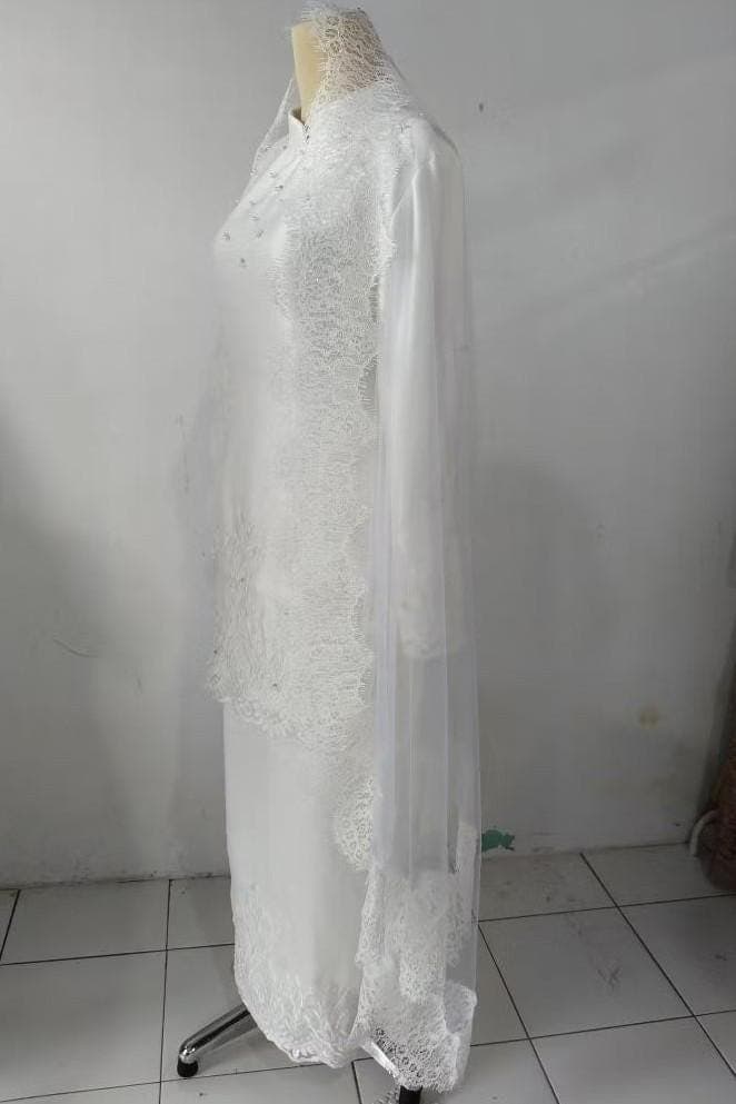 White long-sleeve formal dress with lace and bead embellishments displayed on a mannequin, paired with a matching skirt and veil.