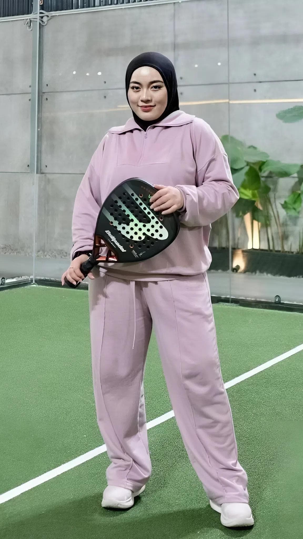 A modest women’s babyterry tracksuit set in dark smokey color, featuring a half-zip top and loose athletic pants, worn on an indoor sports court
