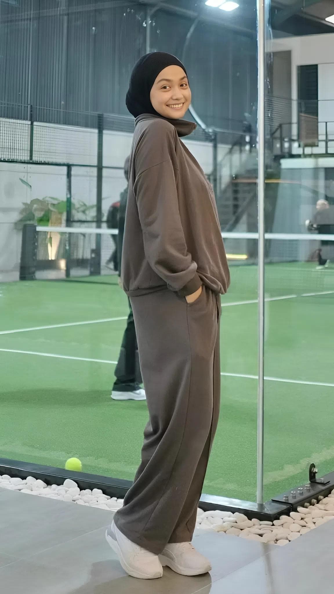 A modest women’s babyterry tracksuit set in dark smokey color, featuring a half-zip top and loose athletic pants, worn on an indoor sports court