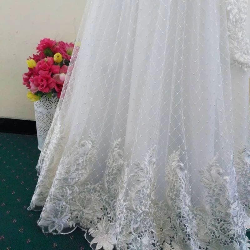 White embroidered lace wedding dress with long sleeves, floral appliqué, and flowing tulle skirt displayed on a mannequin.