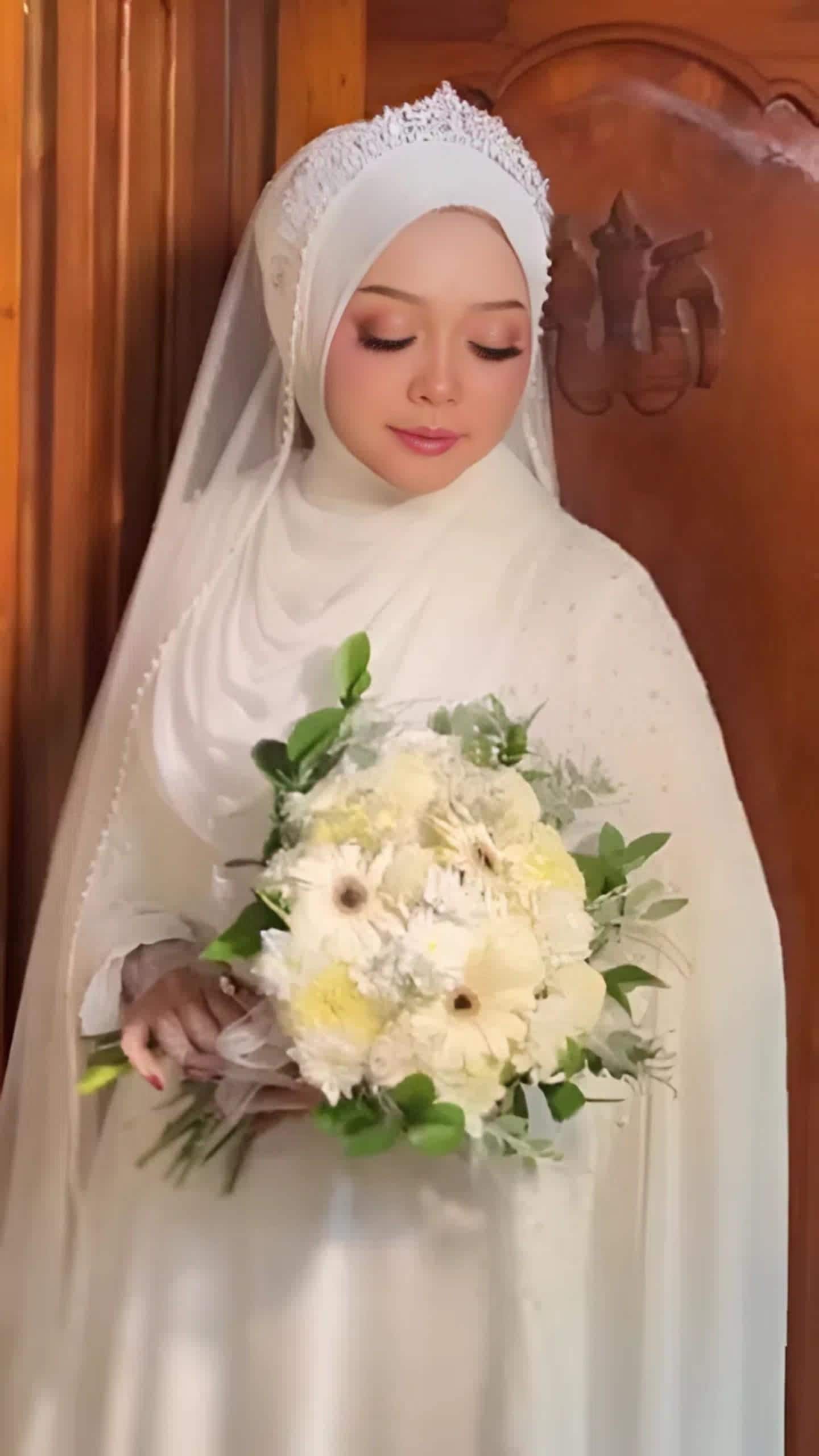 Minimalist white silk abaya wedding dress with flowing cape and matching hijab worn indoors, styled for a modest bridal look.