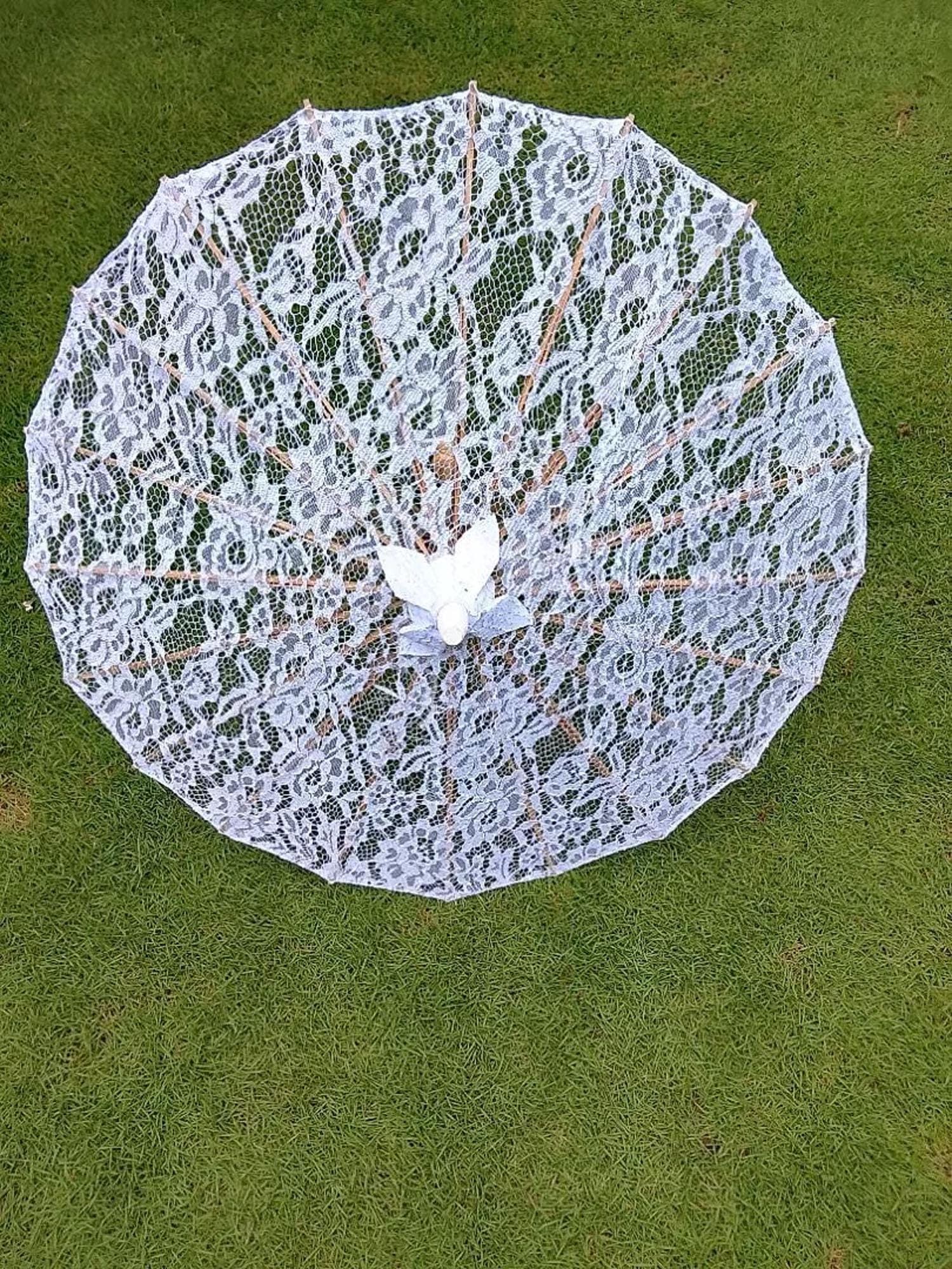 White lace parasol with wooden handle displayed open on grass, showing floral lace pattern and bamboo frame.
