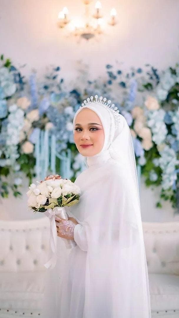 Minimalist white silk abaya wedding dress with flowing cape and matching hijab worn indoors, styled for a modest bridal look.