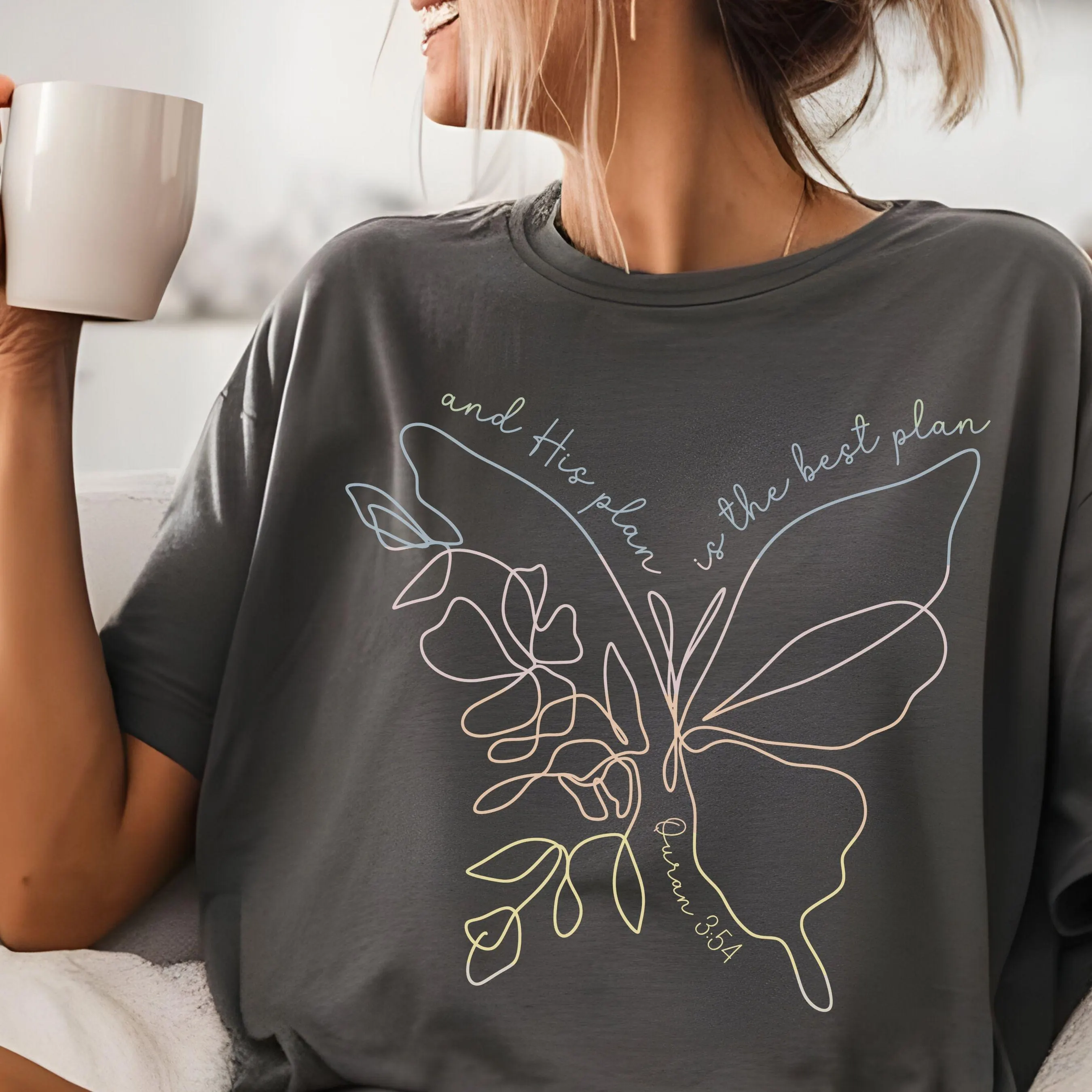 May include: Dark gray t-shirt featuring a butterfly design with the text "and His plan is the best plan" and "Quran 354". The butterfly design is outlined in white, pink, and yellow.