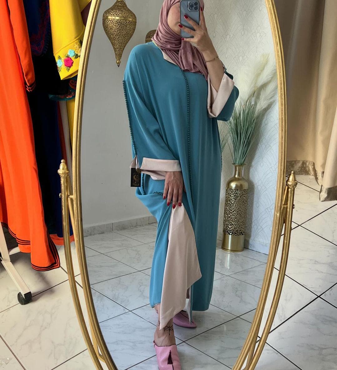 Mirror view of the teal green djellaba alongside other clothing items on a rack