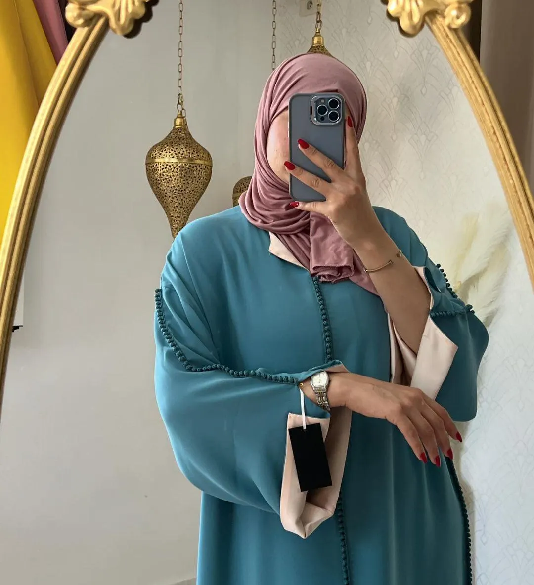 Mirror selfie of the teal green djellaba with pink trim, model wearing a pink hijab