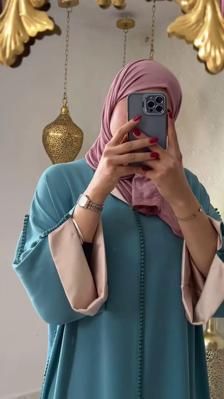 Close-up mirror selfie showing the pink trim detail on the teal green djellaba