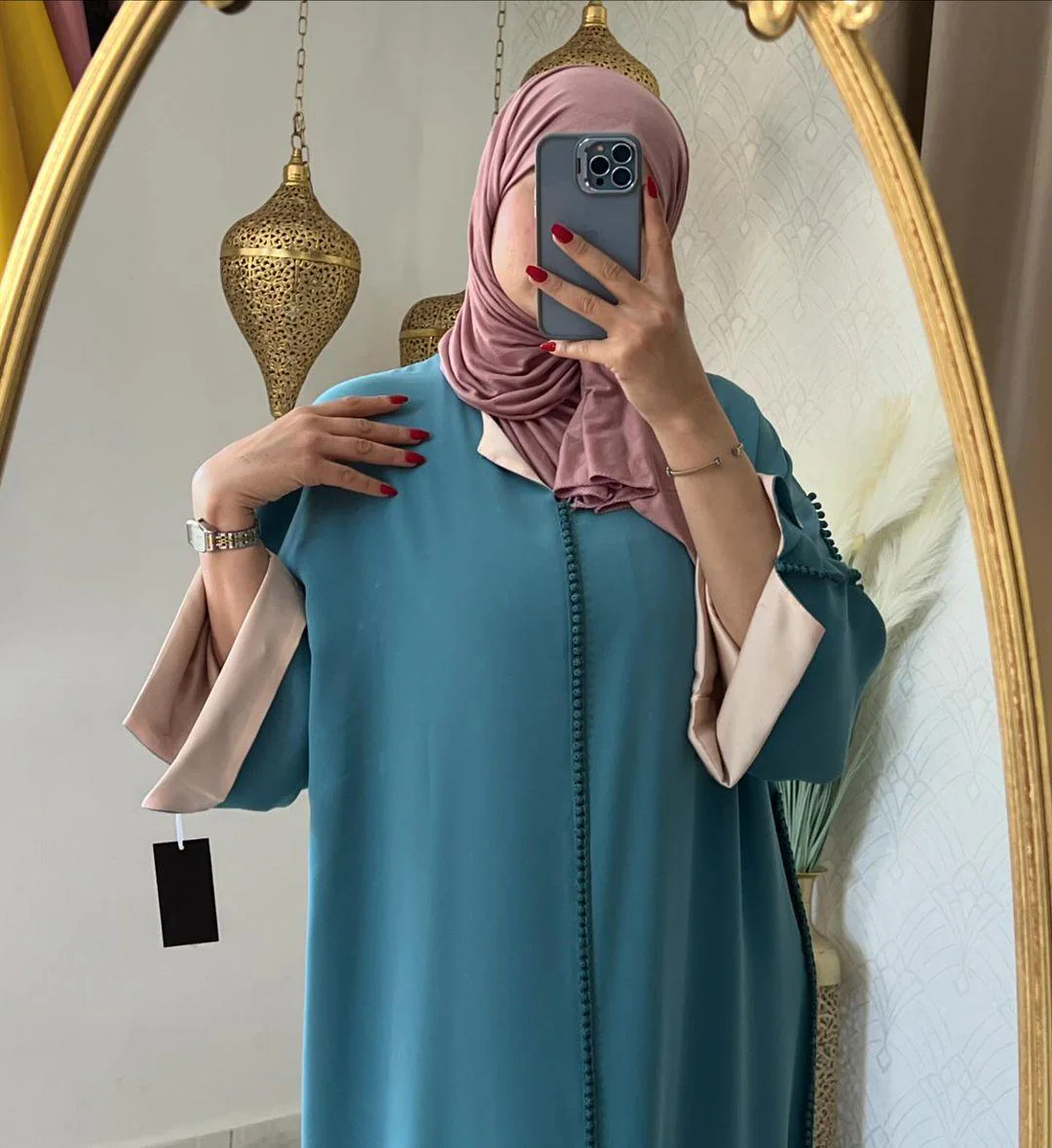 Woman wearing a teal green Moroccan djellaba with pink trim, holding phone for mirror selfie.