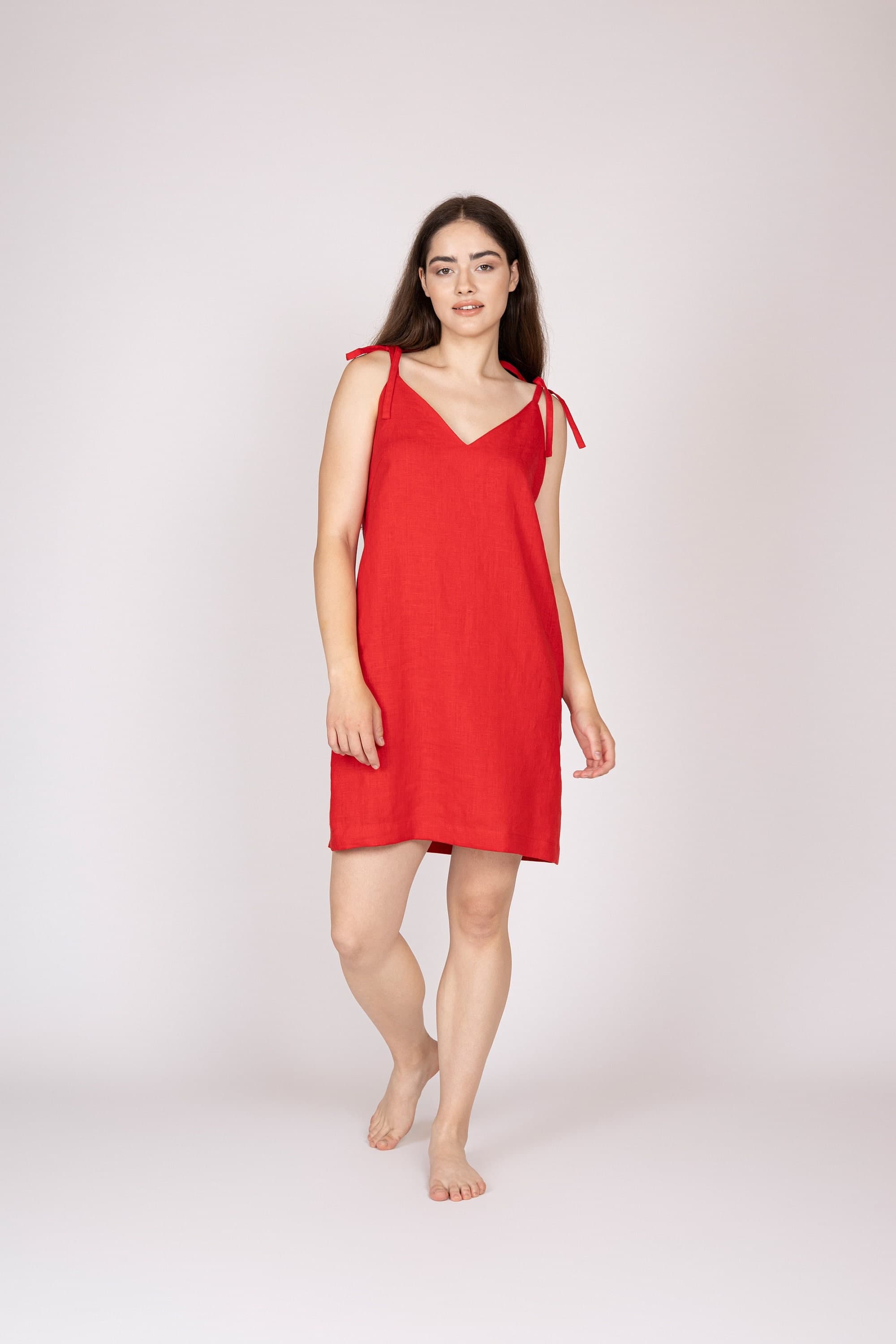 May include: A woman wearing a red linen dress with thin straps that tie at the shoulders. The dress has a v-neckline and a relaxed fit.