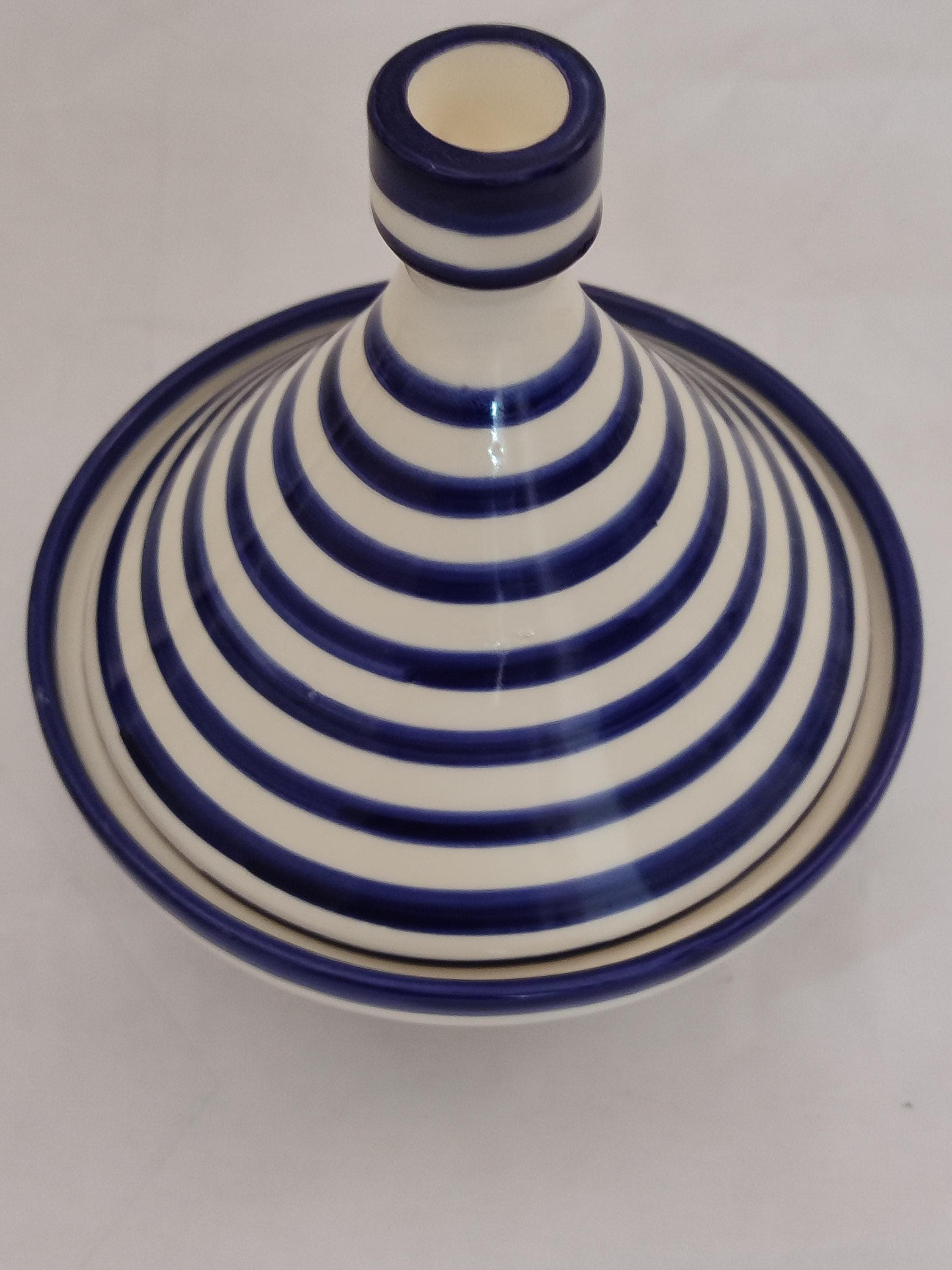 This exquisite blue white Moroccan tagine serves as both functional cookware and stunning table centerpiece. The handmade pottery piece displays bold striped designs characteristic of Fez pottery, with intricate patterns hand-painted using food-safe glazes. The 11" serving tagine comes with matching lid and base plate, perfect for presenting traditional Moroccan dishes in style. Crafted from high-quality ceramic, it's microwave and dishwasher safe (lid removed).