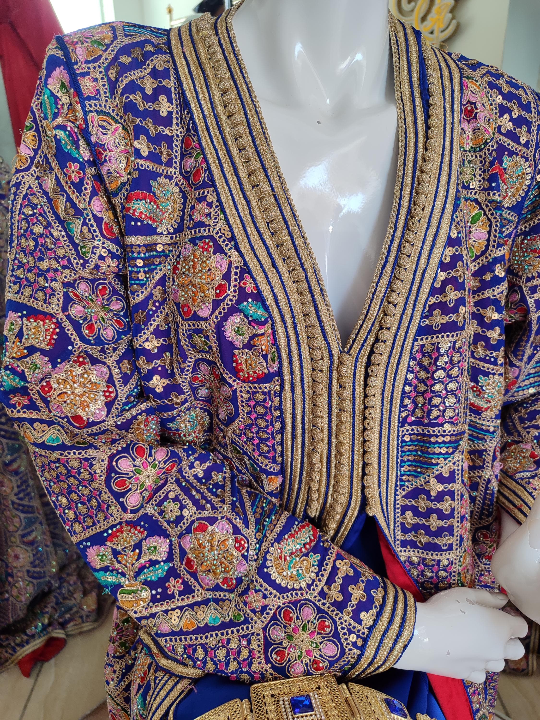 Our luxurious takchita kaftan set redefines bridal elegance with authentic Moroccan craftsmanship. The caftan marocain base layer features delicate lace accents, while the ornate overdress showcases elaborate koftan embroidery techniques. This bridal kaftan is meticulously constructed with premium materials that drape beautifully for a royal appearance. The takchita dress includes coordinating belt and can be customized in various colors.