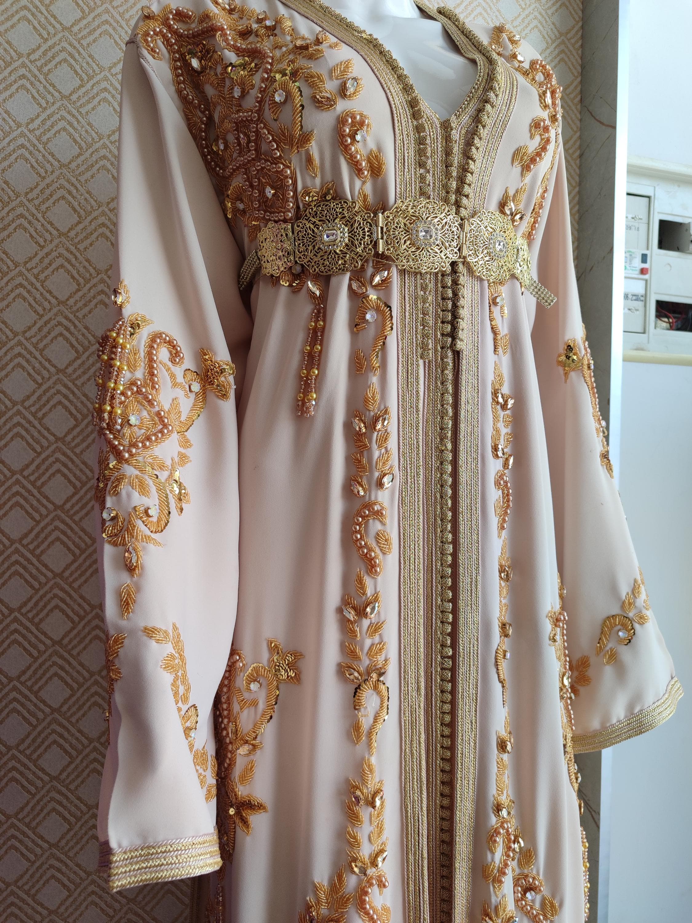 This moroccan takchita set represents the pinnacle of bridal kaftan dresses. The luxurious two-piece design features a dazzling embellished kaftan overlay atop a refined underdress. Hand-sewn with metallic threads and delicate beading, this caftan marocain transforms any nikah into a royal affair. The flattering silhouette works beautifully as both a muslim nikah dress and reception gown. Each stitch honors Morocco's rich textile heritage while offering contemporary bridal sophistication.
