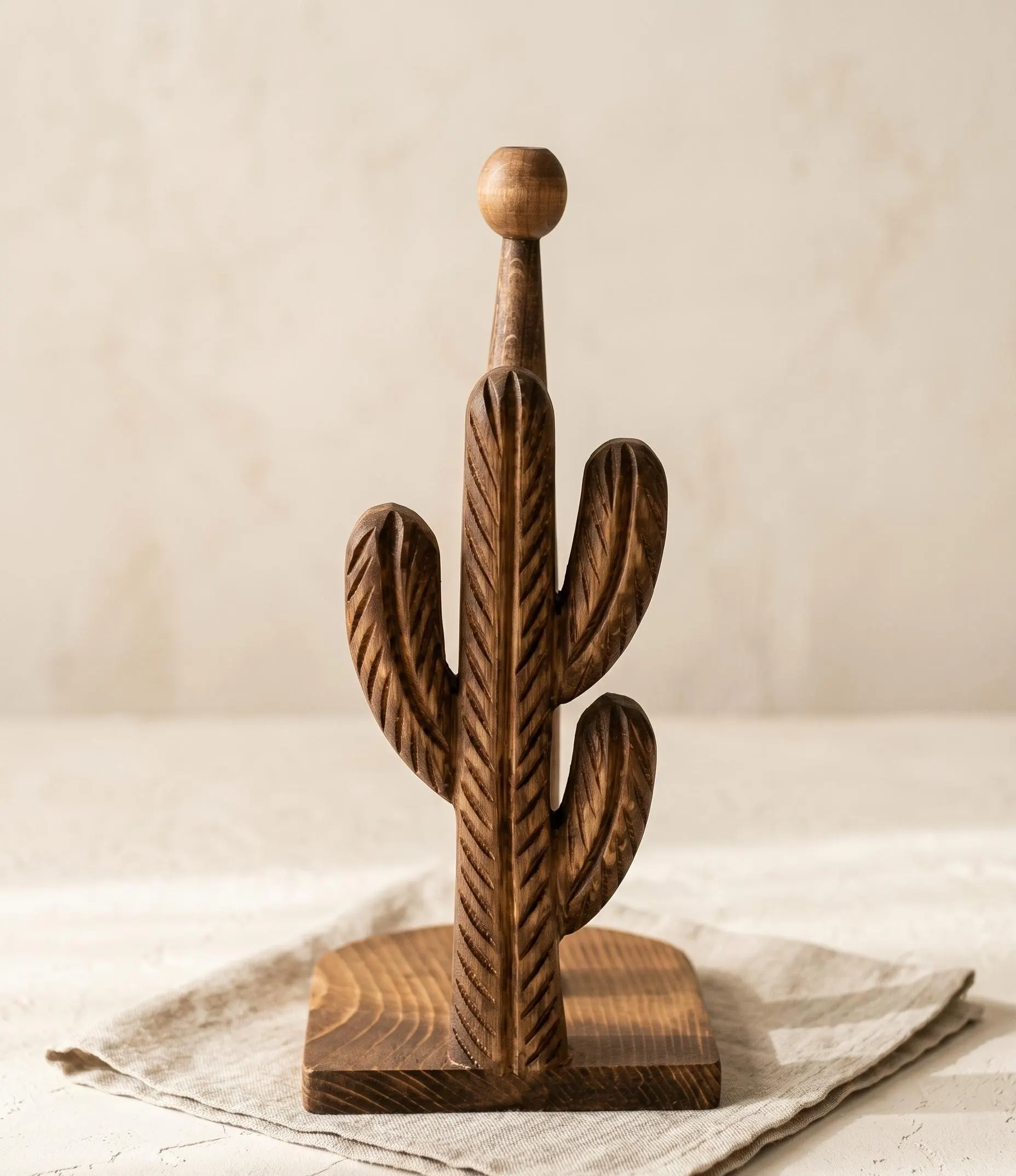 Handcrafted wooden cactus paper towel holder with white paper towel roll on rustic farmhouse wooden table in warm natural sunlight.