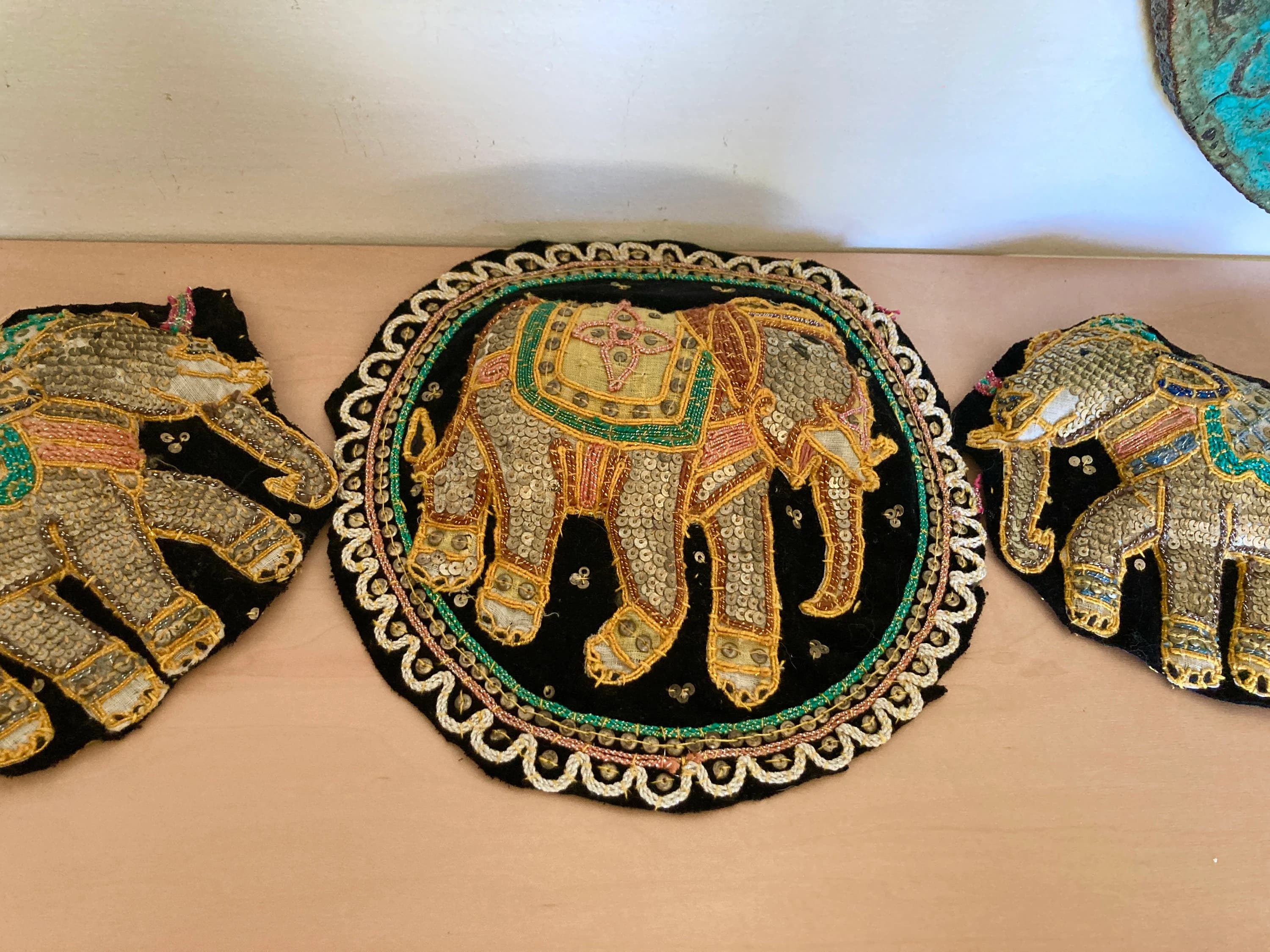 May include: Three decorative elephant appliqués. The elephants are embellished with sequins and beads in gold, silver, pink, and green. They are set against a black background. The central elephant is circular, while the others are shaped.