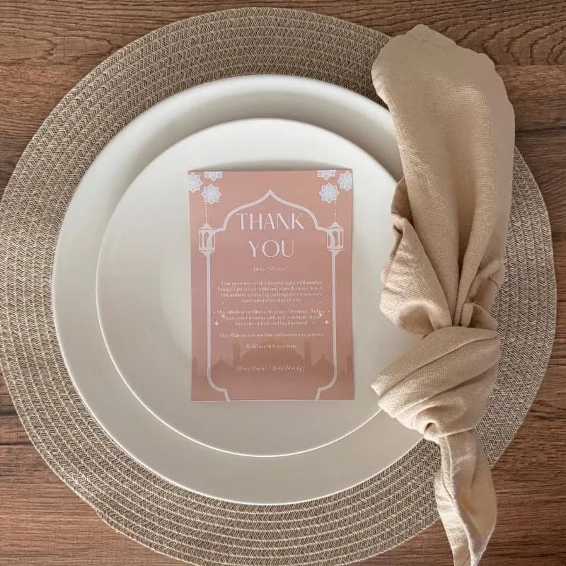 Ramadan thank you card placed on elegant dinner plate with woven placemat and neutral napkin. Printable Islamic appreciation card for Iftar dinner guests. Beautiful decor and stationery for Muslim celebrations, Eid gatherings, and Ramadan events. Includes customizable template for personalized messages. Perfect for adding a thoughtful touch to your Ramadan party table setting or virtual thank you notes.