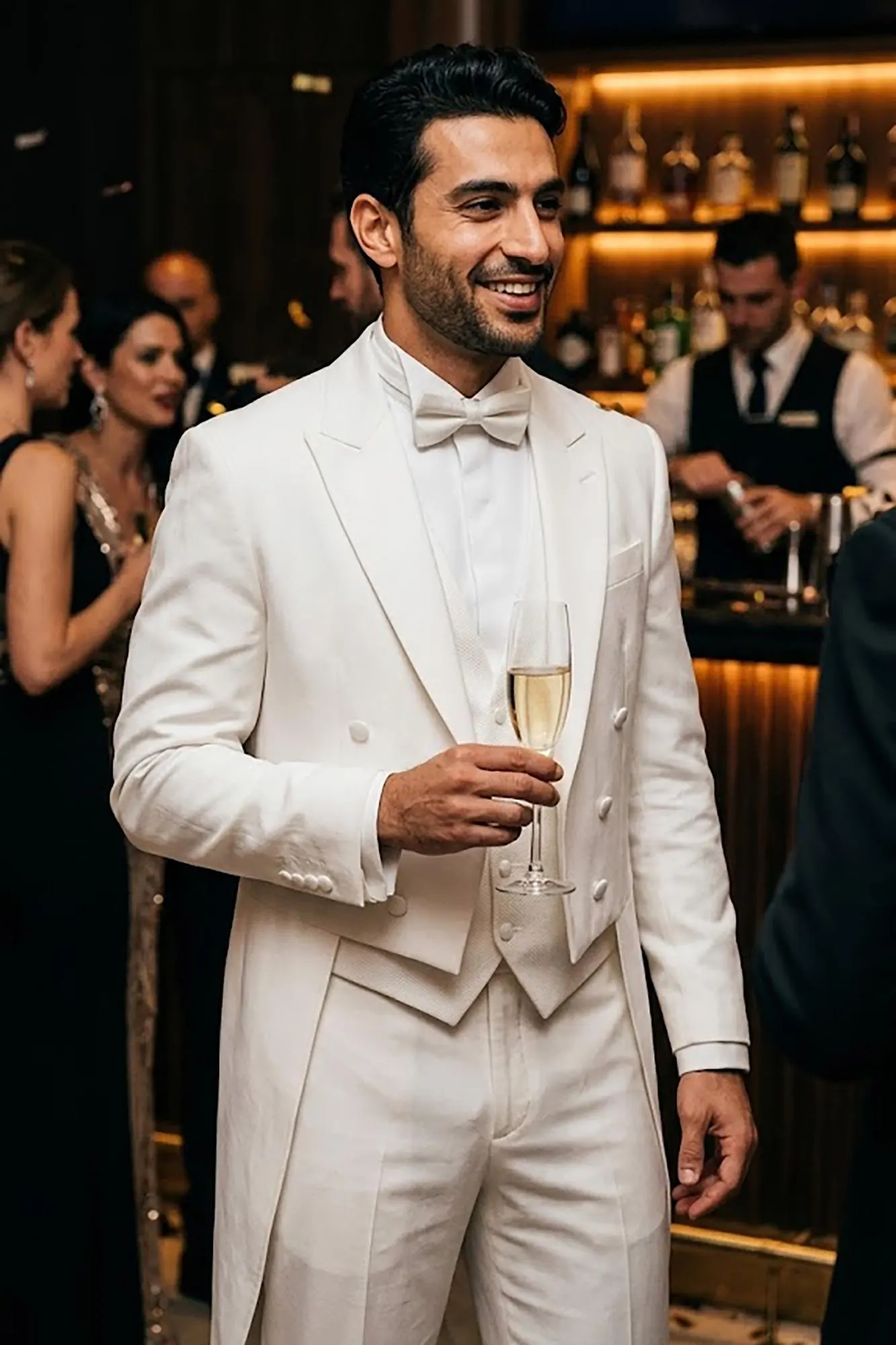A man walking down a hallway wearing a sophisticated black formal tailcoat tuxedo with white trousers and a bowtie