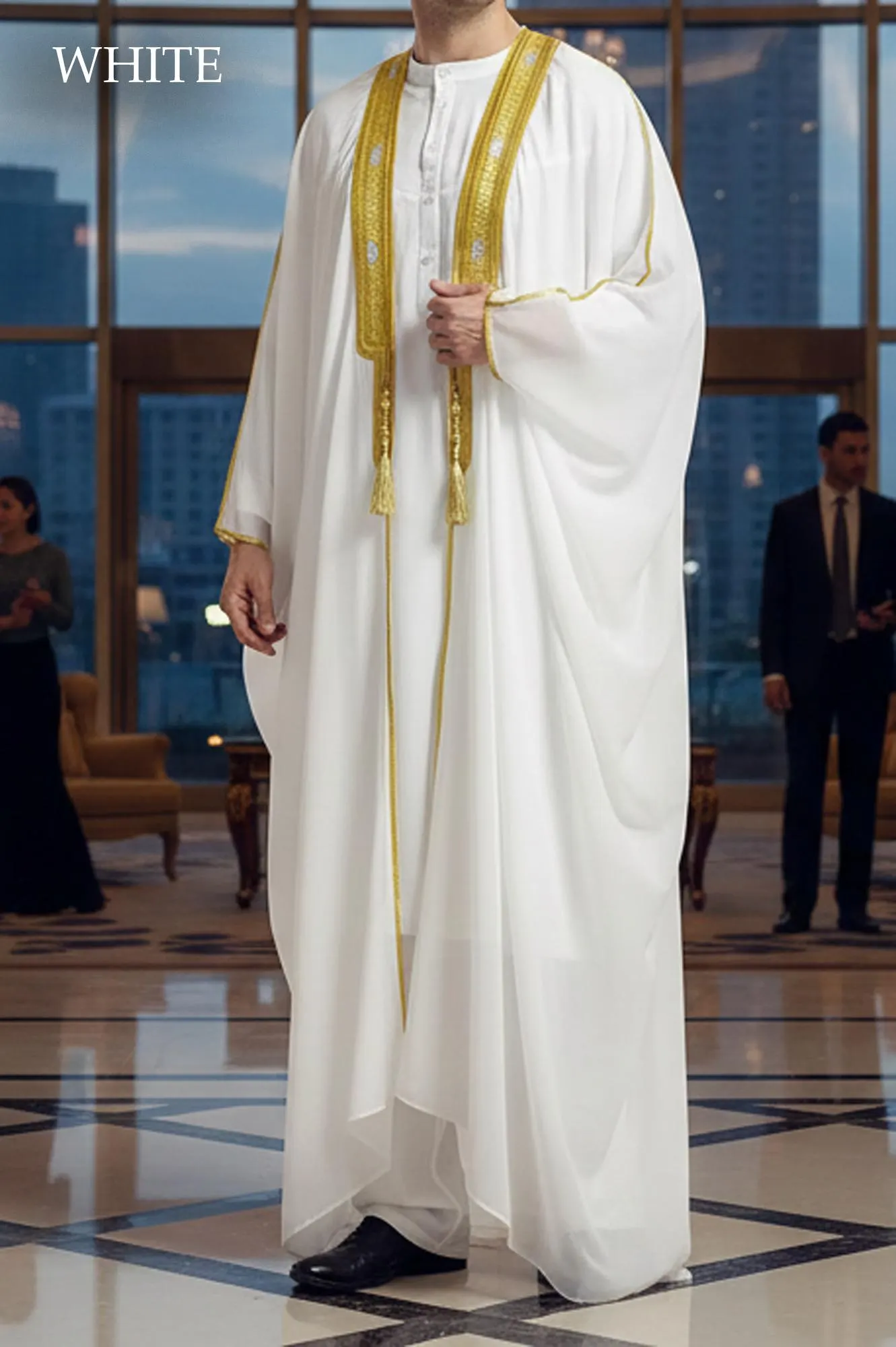 Man wearing a white sheer open-front Bisht robe with gold embroidery on the collar over a white thobe