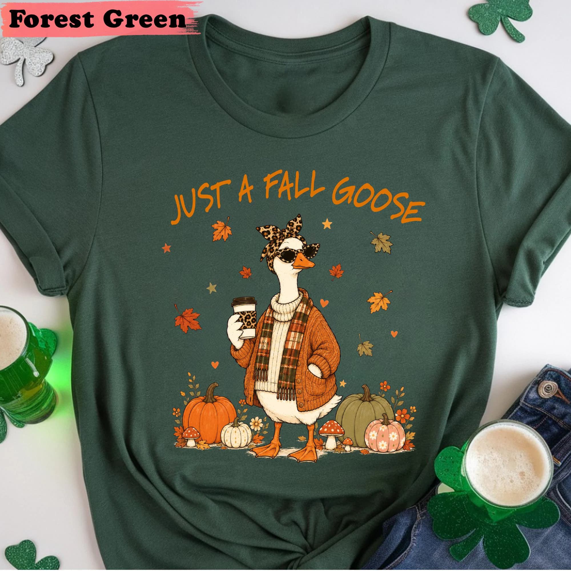 A green t-shirt with a cartoon image of a goose wearing sunglasses and holding a coffee cup, surrounded by autumn decorations like pumpkins and leaves.