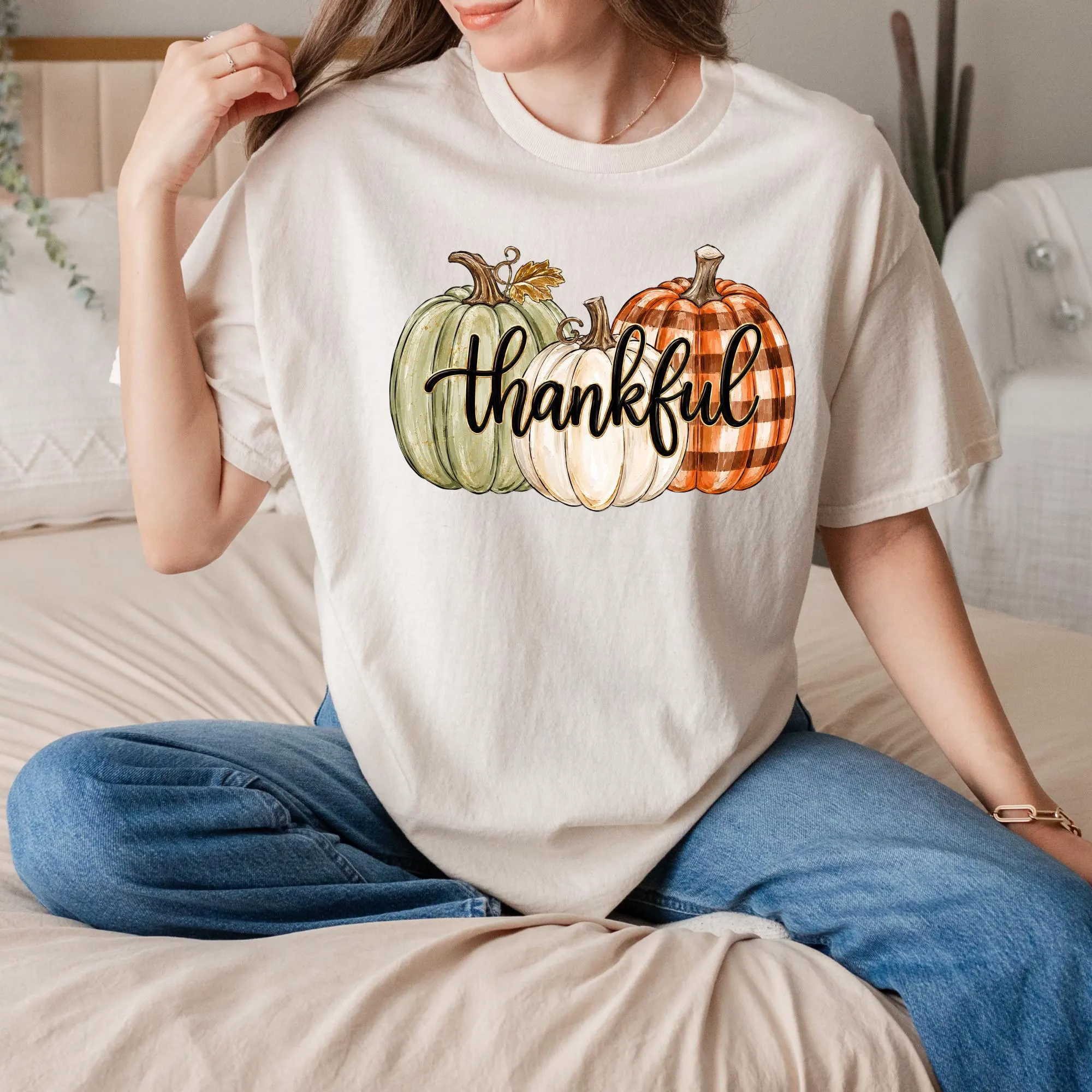 A woman wearing a white t-shirt with a graphic design of three pumpkins and the word "Thankful" printed on it.