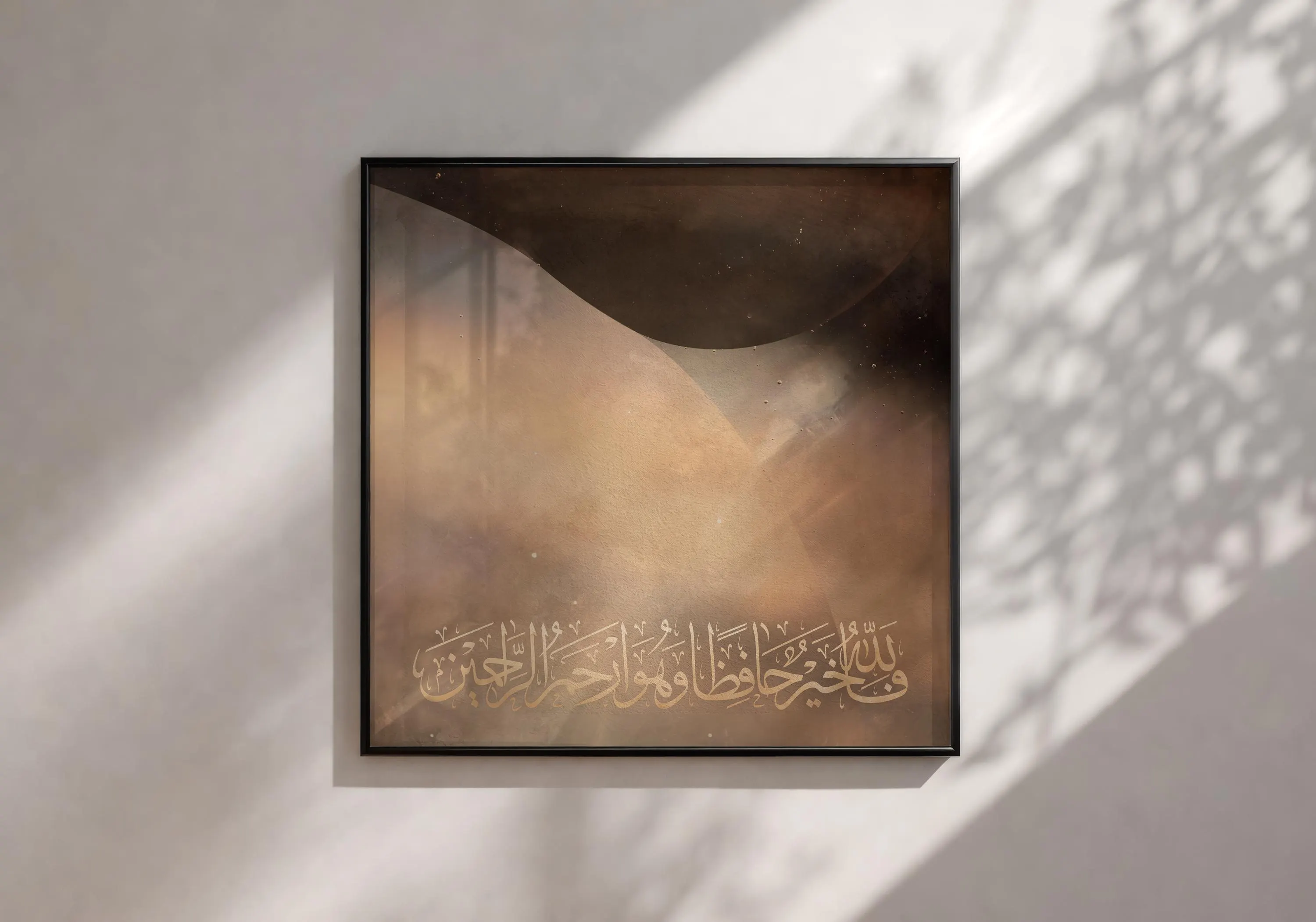 May include: Square framed artwork with a dark brown and beige abstract design. The artwork features gold Arabic calligraphy at the bottom. The frame is black. The artwork is on a white wall.