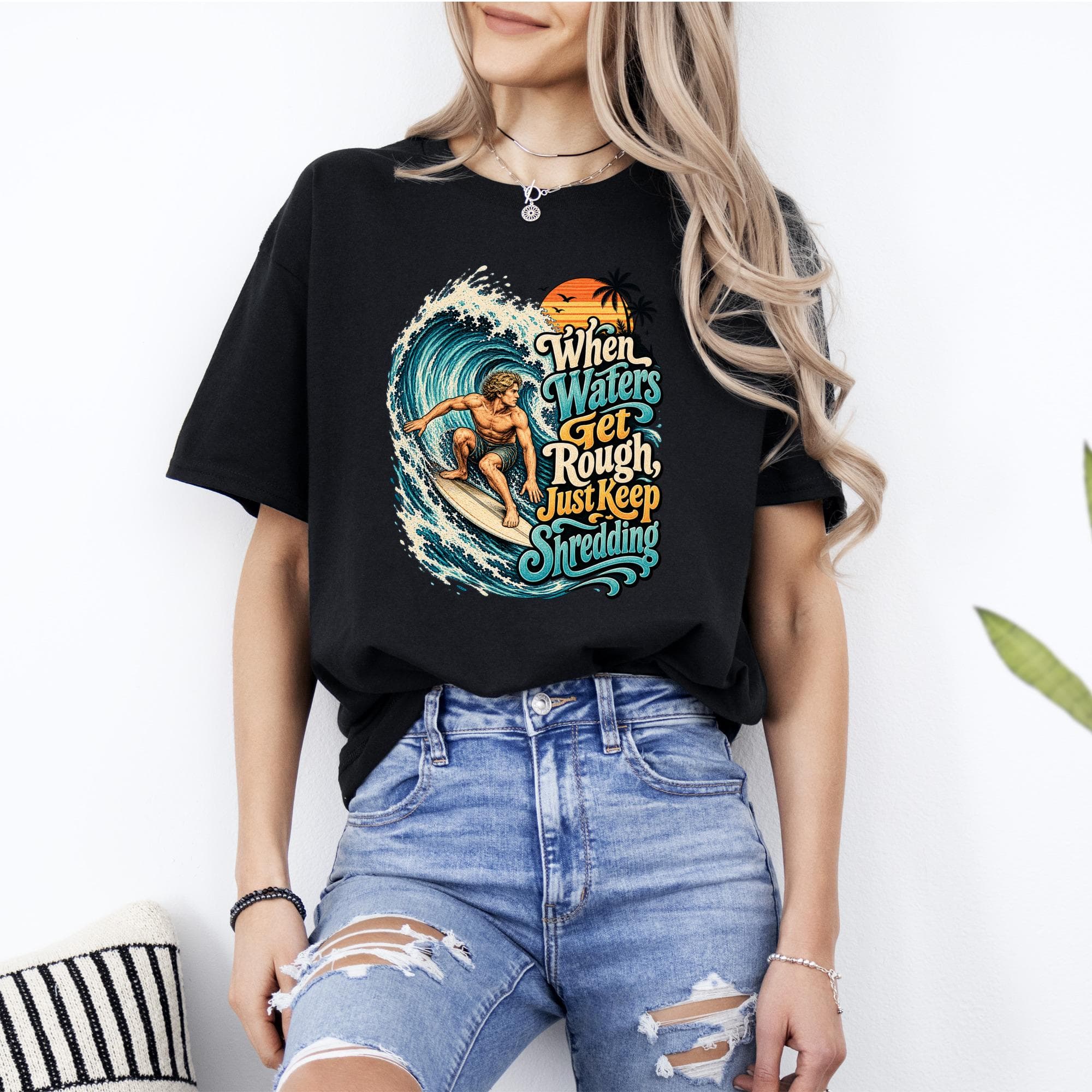 Black t-shirt graphic with surfer on a wave and text "When Waters Get Rough, Just Keep Shredding".
