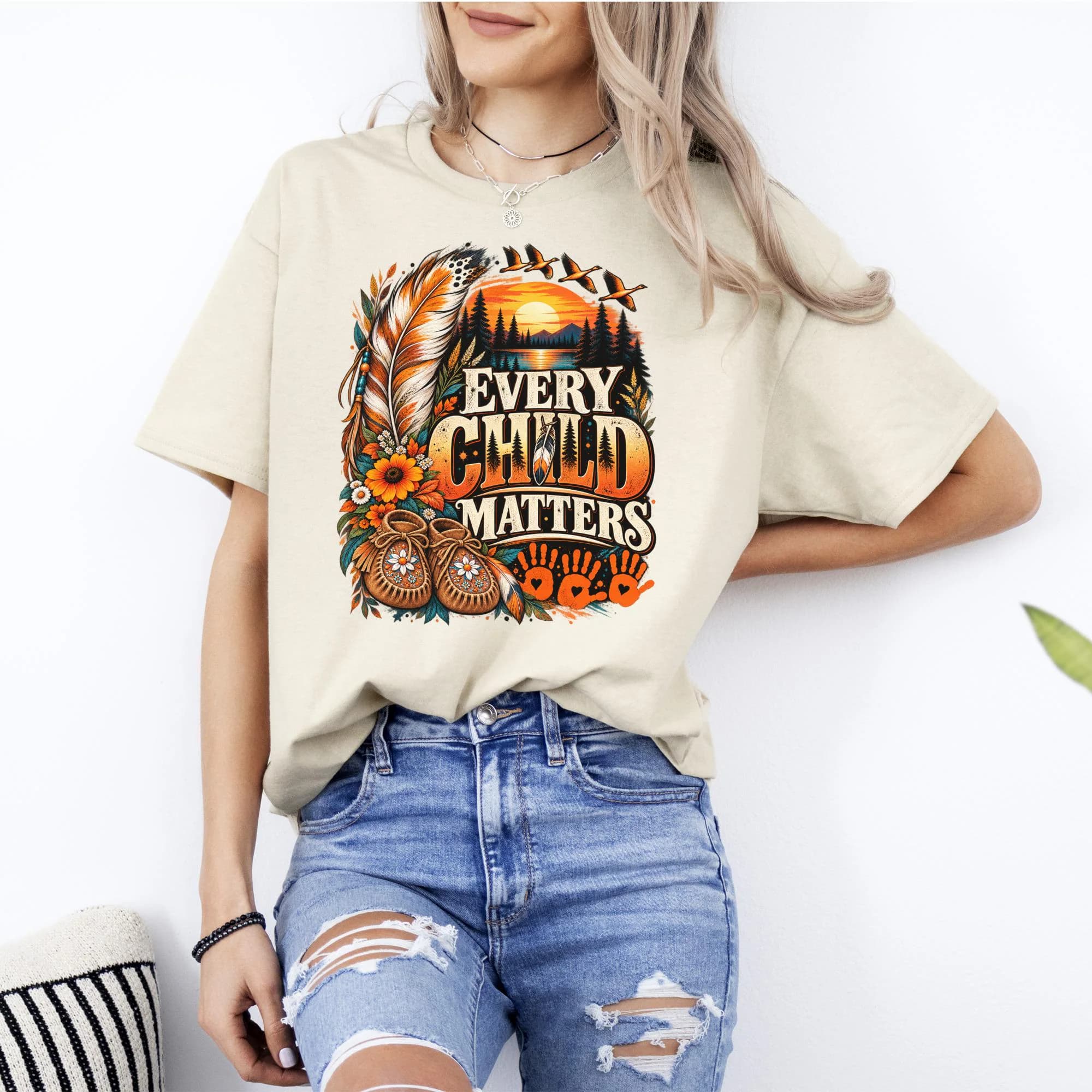 T-shirt graphic with "EVERY CHILD MATTERS" text, feathers, moccasins, and sunset landscape.