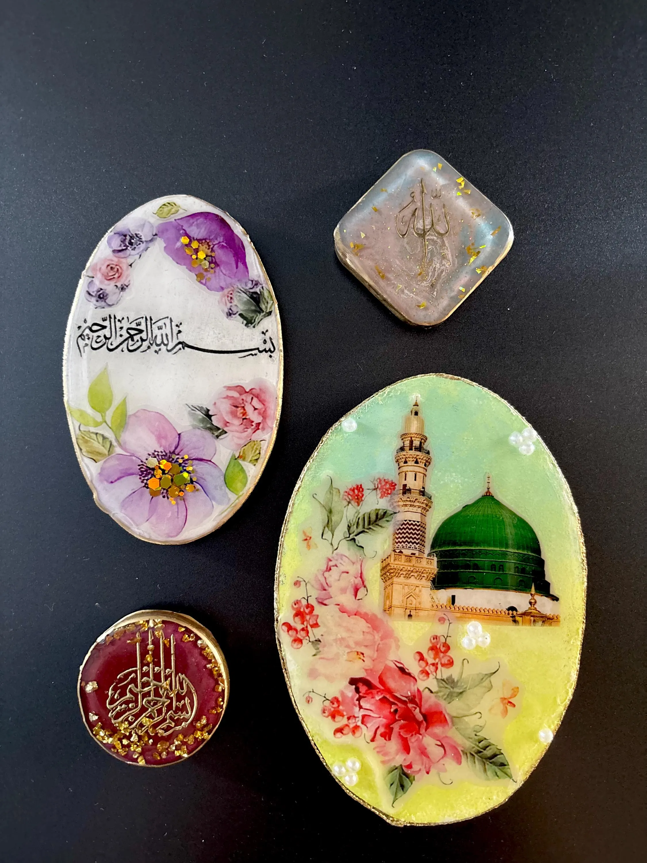 Handcrafted Islamic resin art pieces on a black background, featuring floral designs, Arabic calligraphy, gold foil accents, and a green dome mosque illustration, arranged as decorative keepsakes.