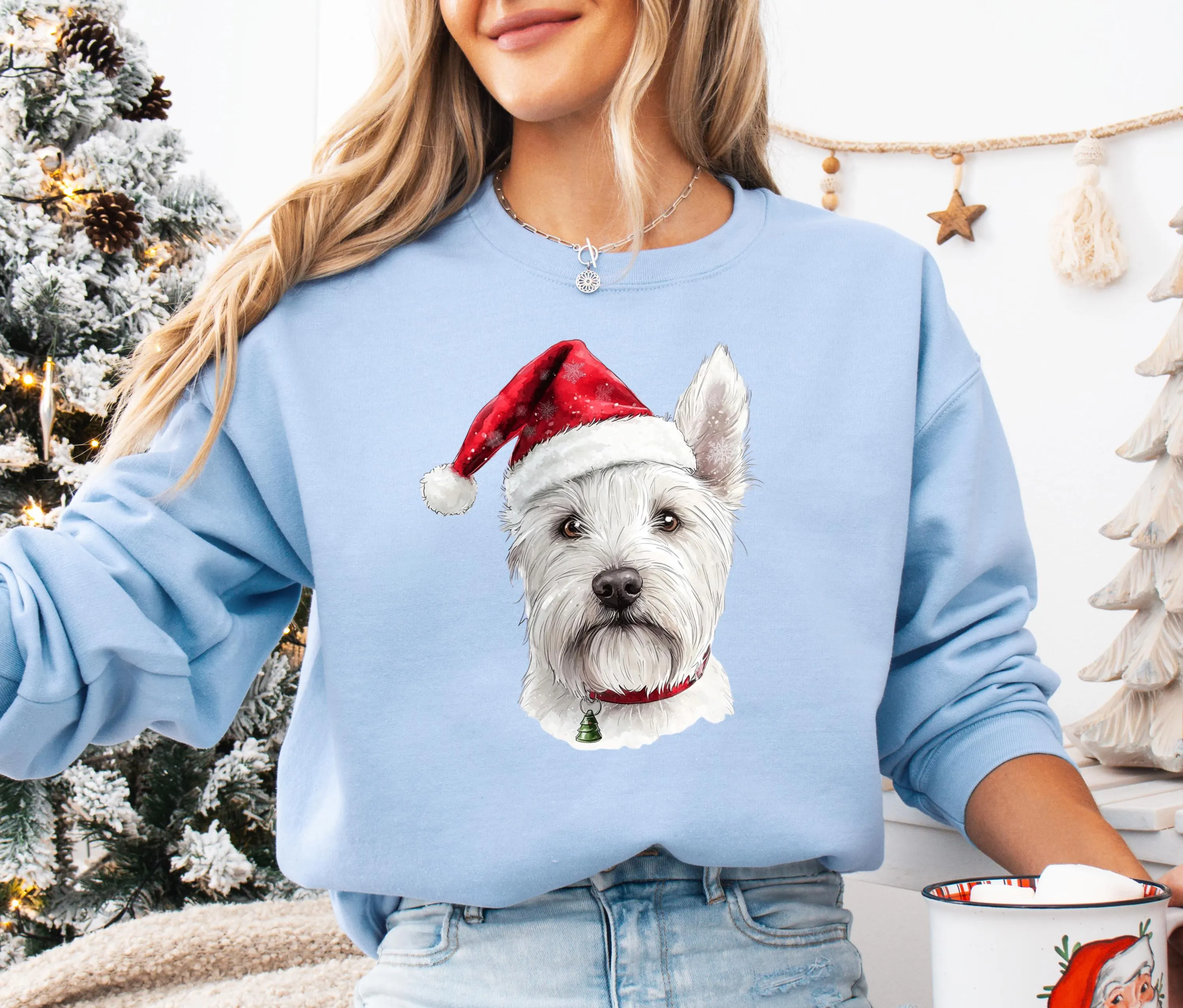 A woman wearing a blue sweatshirt with a white dog wearing a Santa hat.