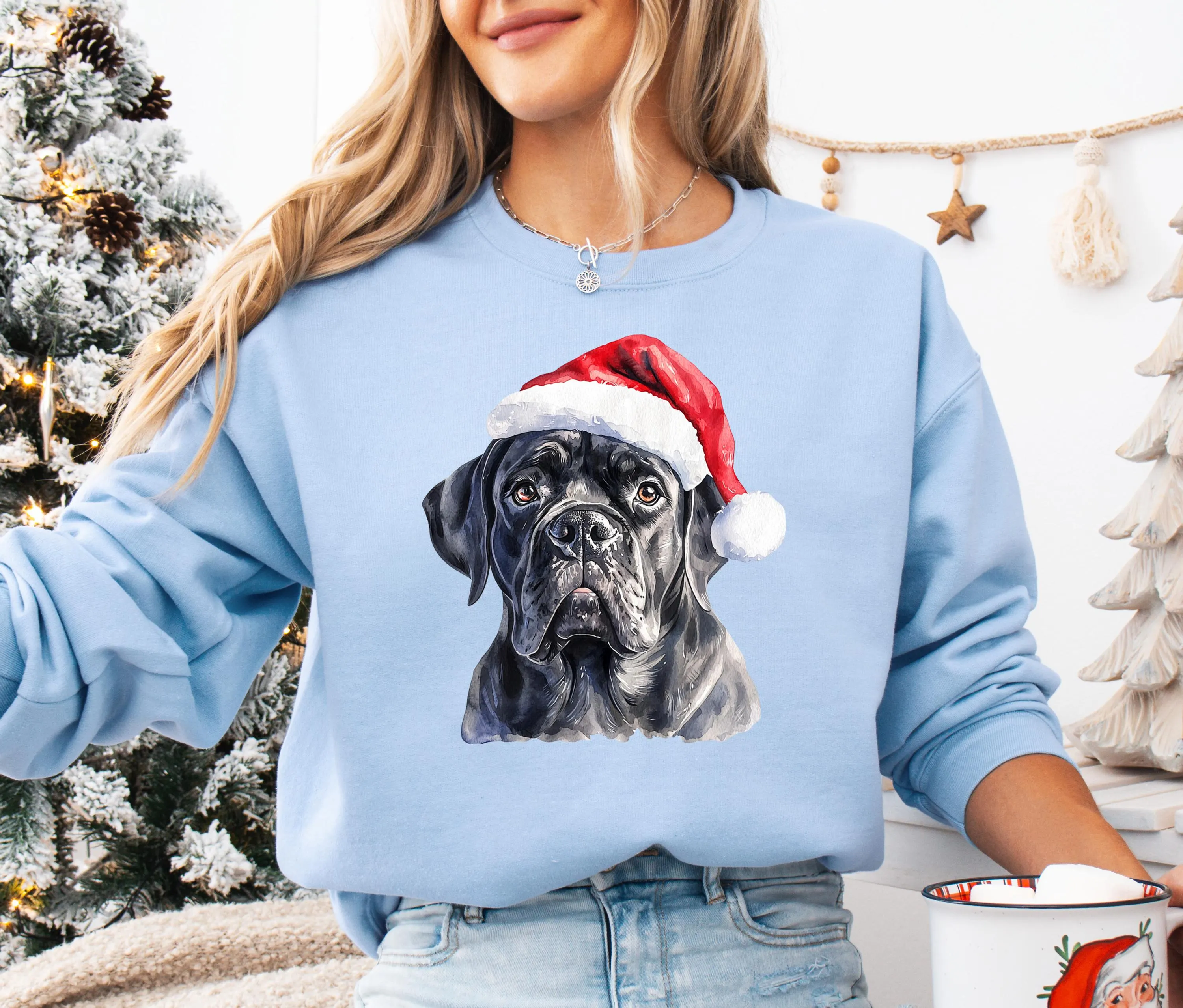 A woman wearing a blue sweatshirt with a black dog wearing a Santa hat.
