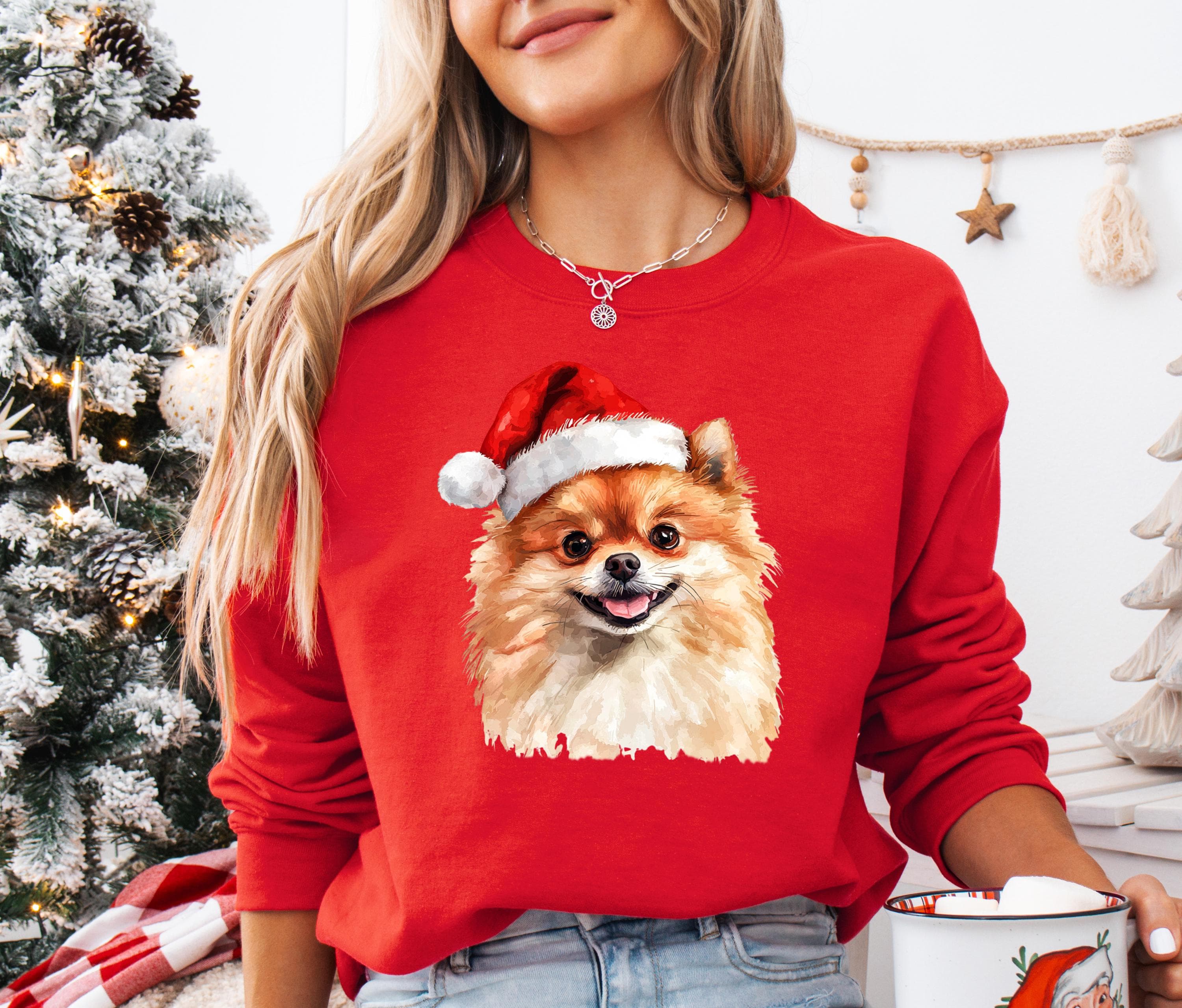 A woman wearing a red sweater with a Pomeranian dog wearing a Santa hat, standing in front of a Christmas tree.