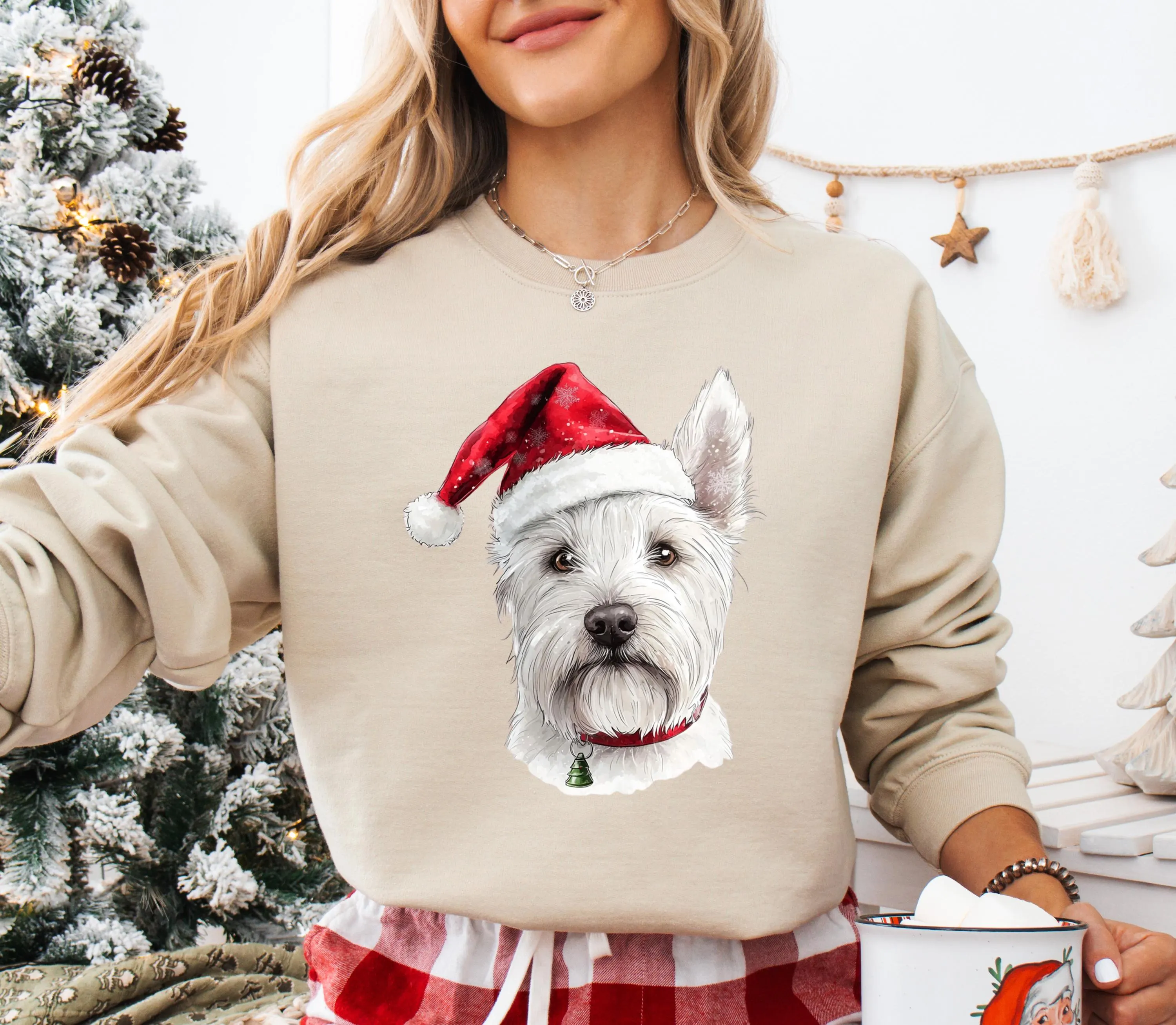 A woman wearing a beige sweater with a white dog wearing a Santa hat printed on it, standing in front of a Christmas tree.