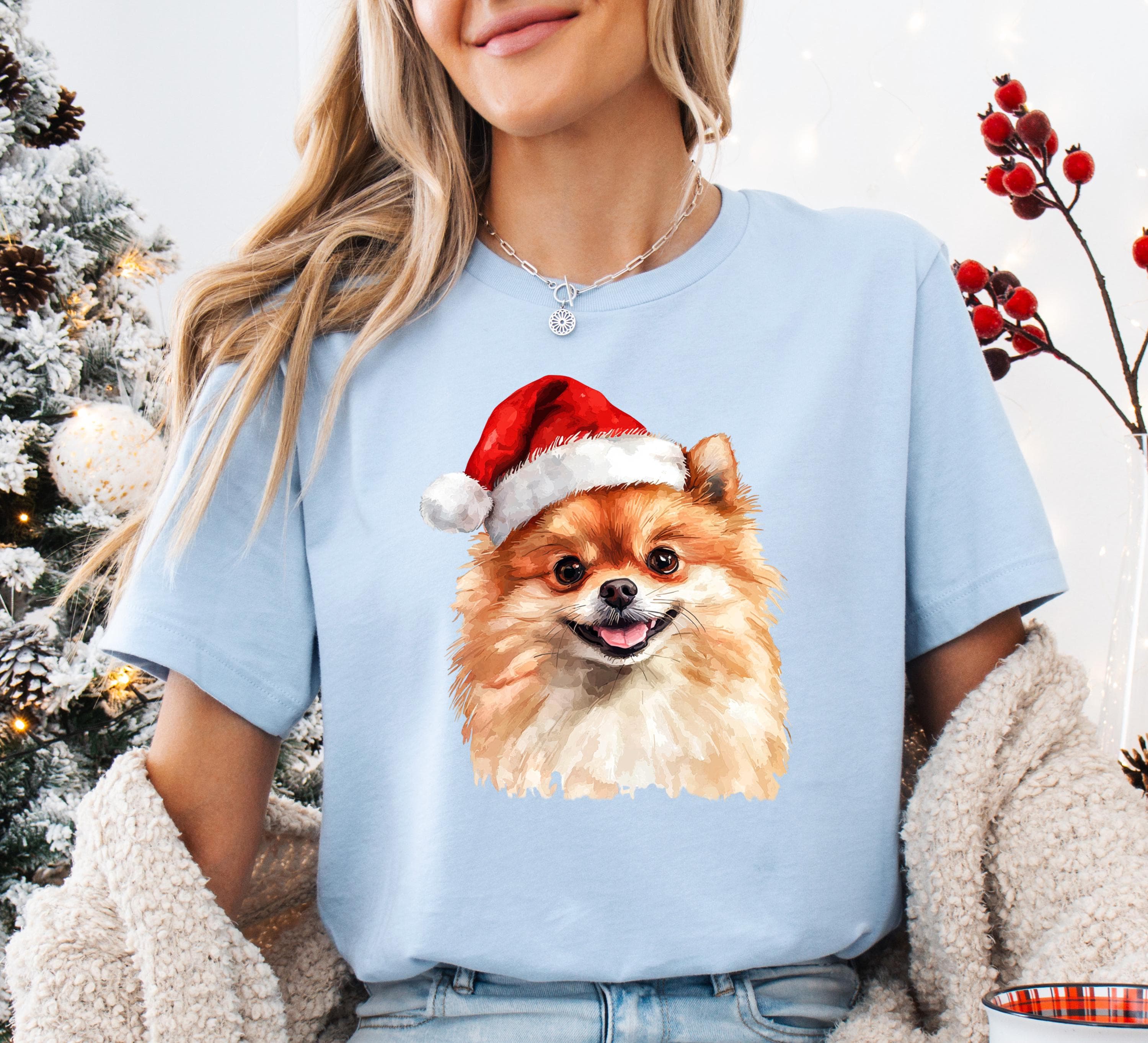 A woman wearing a light blue t-shirt with a picture of a Pomeranian dog wearing a Santa hat.