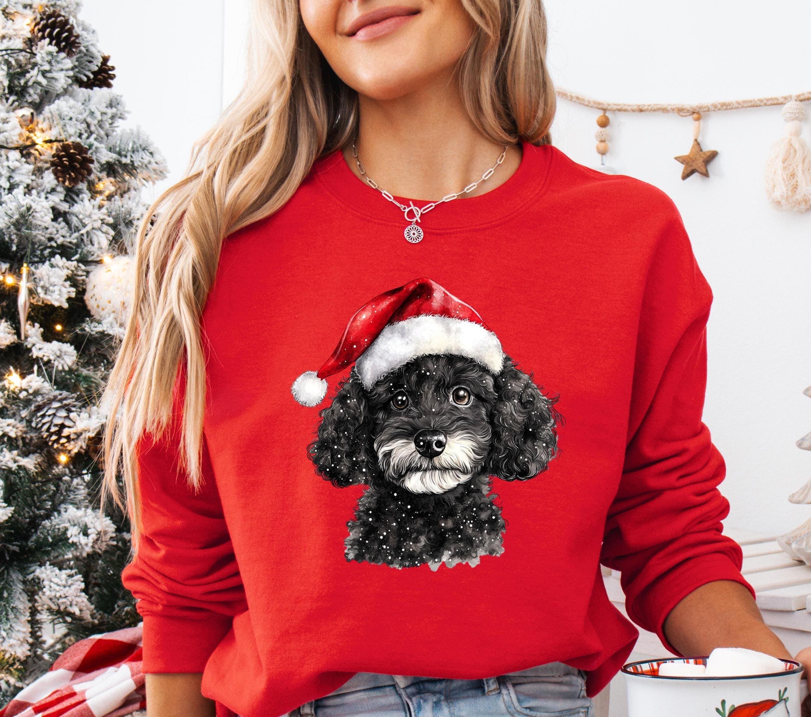 A woman wearing a red sweater with a black dog wearing a Santa hat, standing in front of a Christmas tree.