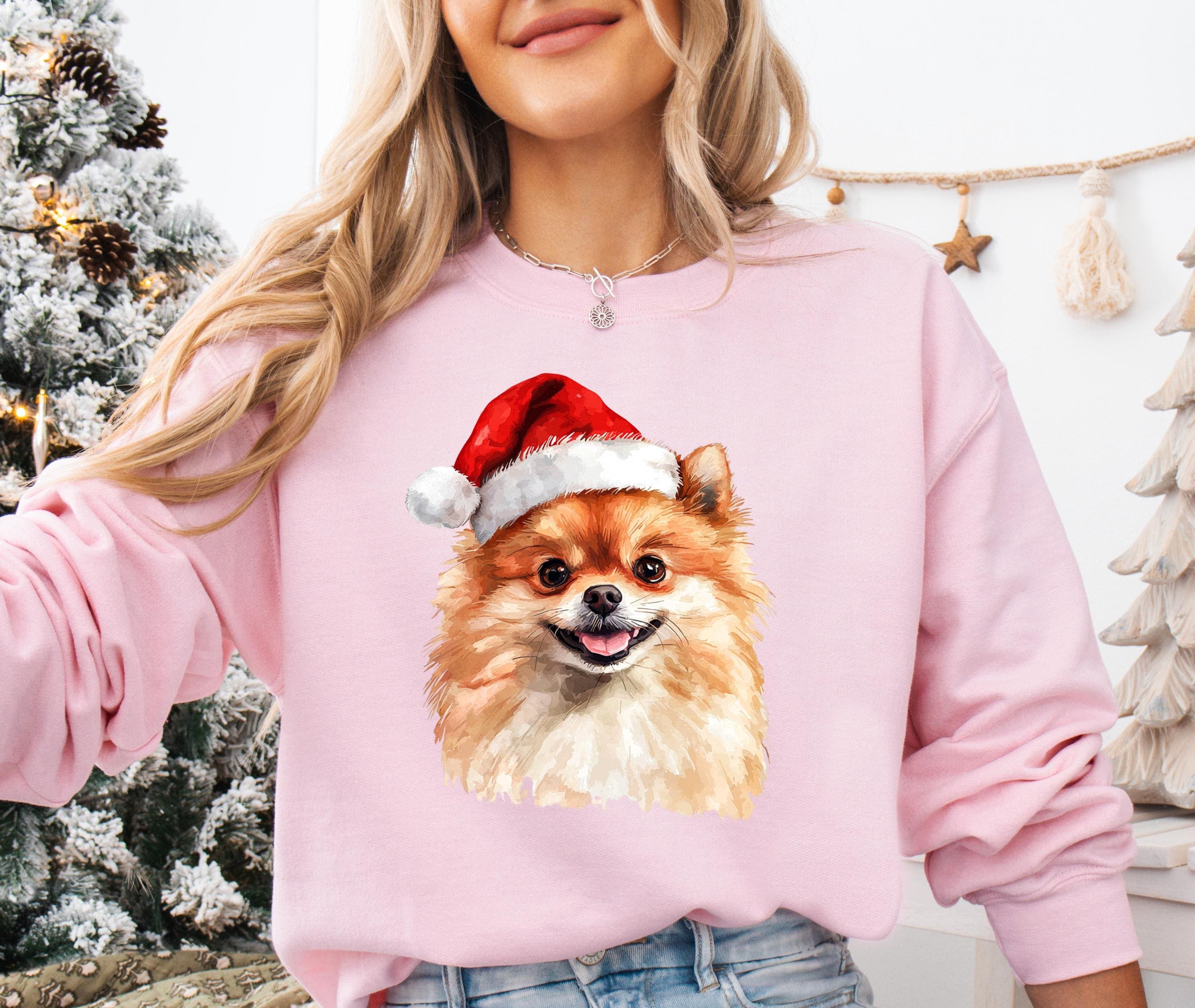 A woman wearing a pink sweatshirt with a picture of a Pomeranian dog wearing a Santa hat.