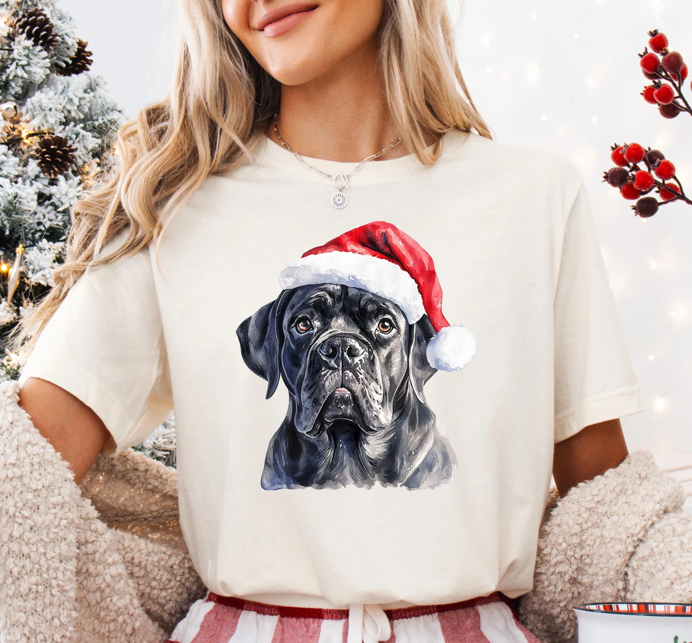 A woman wearing a white t-shirt with a black dog wearing a Santa hat.