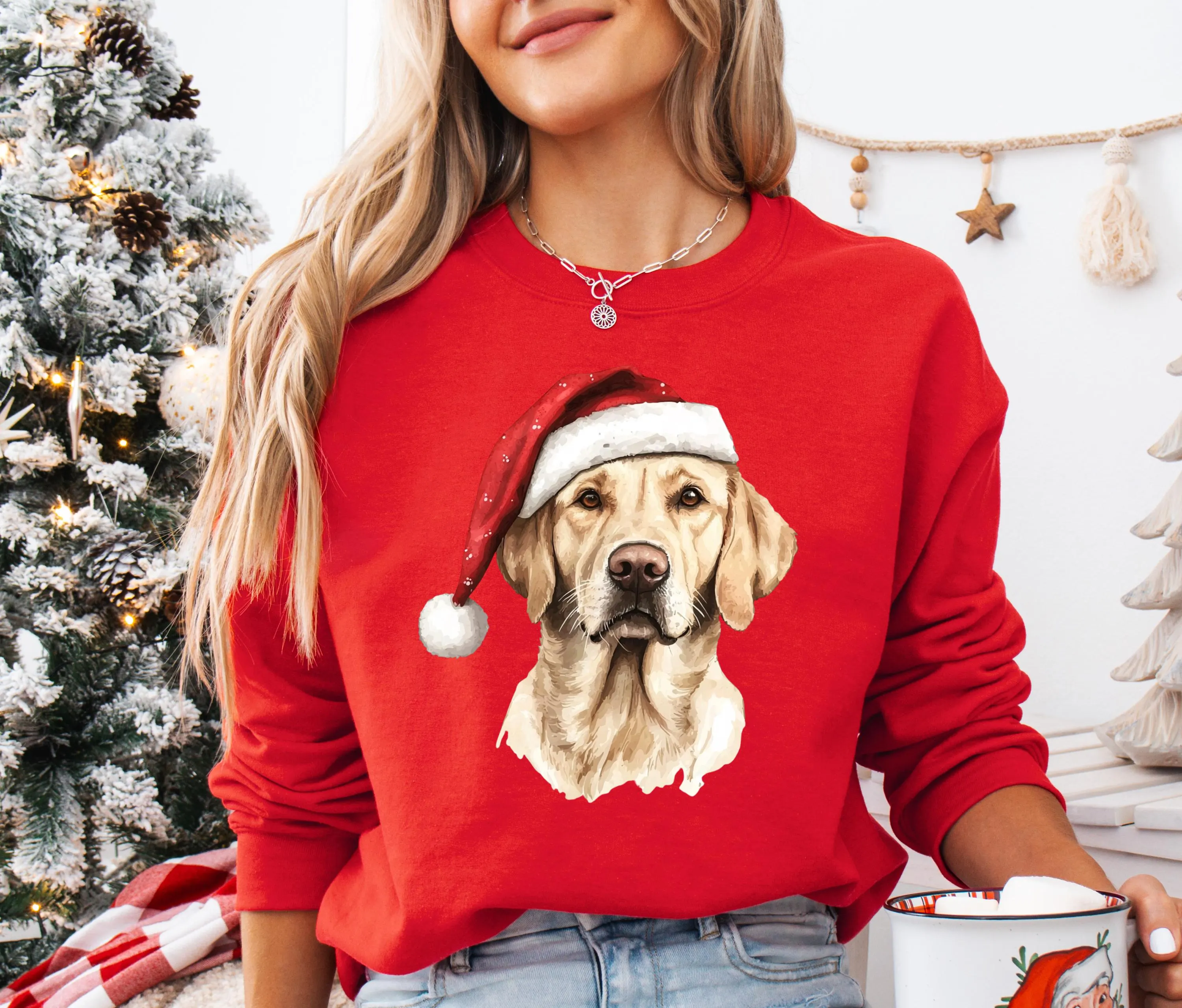 A woman wearing a red sweater with a dog wearing a Santa hat is standing in front of a Christmas tree.