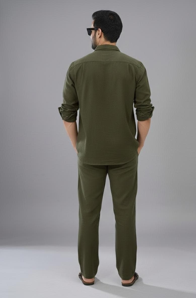 May include: Olive green shirt and trousers set. The shirt features a button-down collar and rolled-up sleeves. The trousers are straight-legged. The outfit is made of a lightweight fabric, suitable for warmer weather.