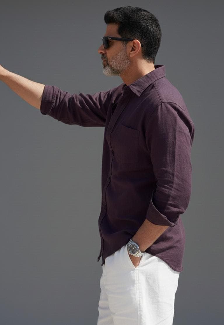 May include: A dark purple shirt with a chest pocket and rolled-up sleeves, paired with white trousers. A silver wristwatch is visible. The person is wearing sunglasses. The shirt is buttoned up.