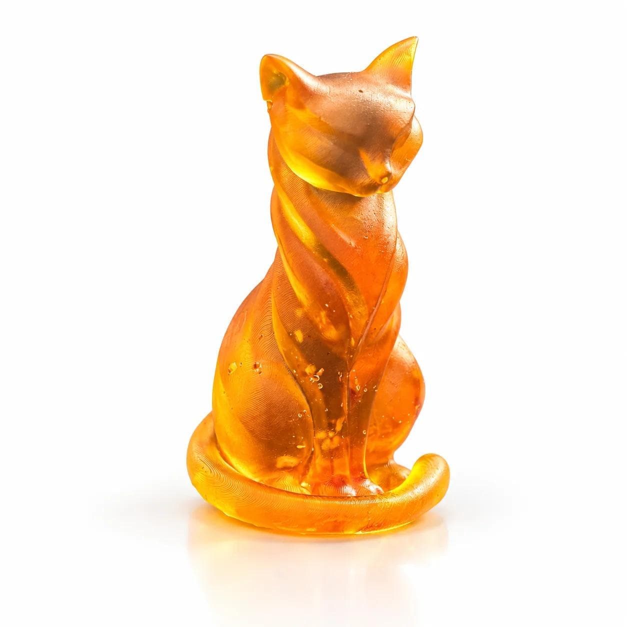 Golden orange slender sitting cat figurine with satin-textured cheeks and translucent body on a white studio background